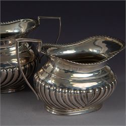 Victorian silver bachelors teapot, of part fluted oval form with ebonised wooden handle and finial, hallmarked Thomas Bradbury & Sons, London 1896, together with a Edwardian silver milk jug and open sucrier, of similar form with oblique gadrooned rims, hallmarked George Unite, Birmingham 1902 & 1906