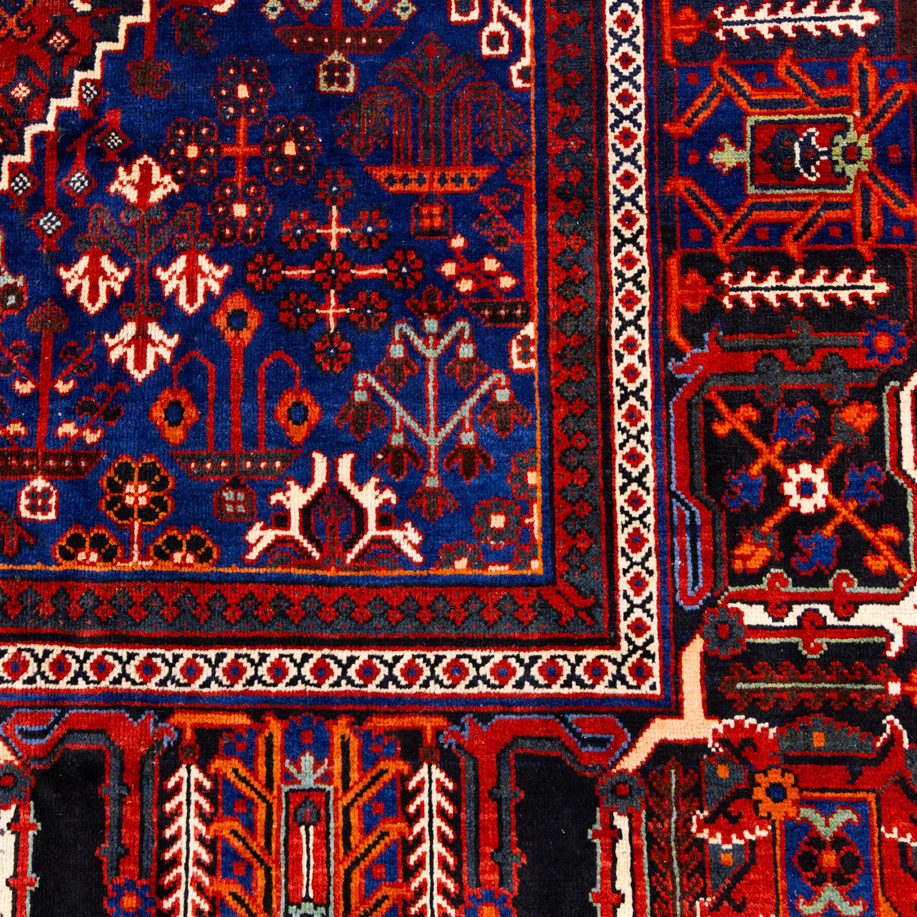 Central Persian Joshagen hand-knotted carpet, madder-red field with a central stepped lozenge medallion and densely filled with stylized geometric floral and tree motifs arranged in a repeating lattice enclosed by indigo spandrels and a broad navy border of angular palmette and vine ornament, flanked by multiple guard stripes, cotton fringe ends 