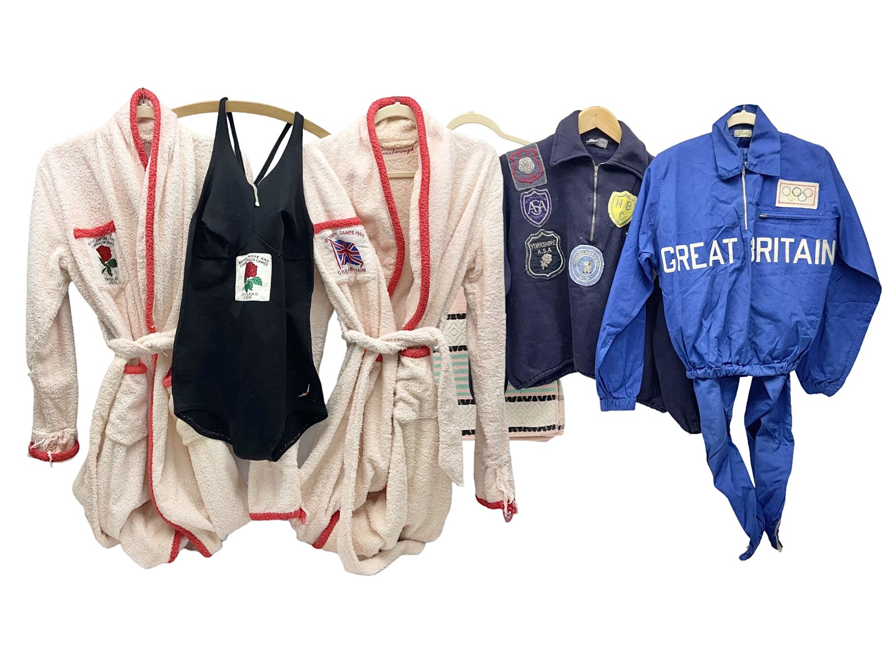 On the direct instructions of Anita Porter nee Lonsbrough Great British Olympic and Commonwealth Games gold medal winning swimmer - collection of early and international memorabilia comprising original Huddersfield Bath Club track suit top bearing eight stitched on cloth badges including British Empire & Commonwealth Games 1958 England Team, YSASA, North Eastern Counties ASA, ESSA Division 3,  English Schools Swimming Association winner etc
The swimming costume Anita wore at the 1958 Commonwealth Games in Cardiff, her first major championships, where she won two gold medals. The grey elastic on the sides, in those days, she would use to make it tighter and more streamlined.
Blue track suit from the 1960 Olympics which she wore on the podium receiving the gold medal.
1960 pool side towelling robe used at the Rome Olympics (interesting to note her name is spelt wrong on the embroidered label).
1962 Commonwealth Games pool side towelling robe used in Perth Australia when winning three Gold medals. 
It was also this year she became BBC Sports Personality of the year, the first female to do so.
Her 'lucky' pool side towel which she took with her to every event she competed in and which can be seen round her neck in many official celebratory photographs. Copies of some of these photographs are included for identification.
In addition there are two souvenir programmes of an evening event to honour Anita at The Theatre Royal Huddersfield and she has kindly signed the front cover on one of these.