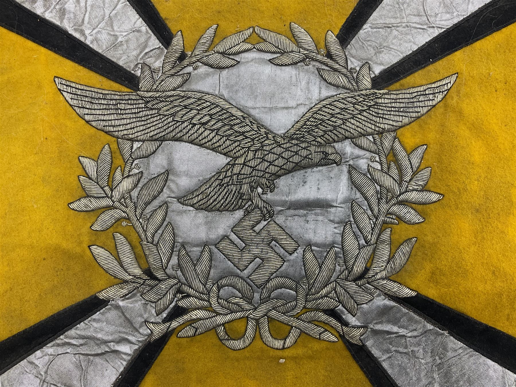 Two replica German Luftwaffe trumpet banners, one heavily silver wire embroidered with Luftwaffe eagle in a wreath, on an amber, white and black rayed background, , with silver wire tasselled border and four leather hanging loops, approx. 50 x 49cm; the other slightly larger heavily gold wire embroidered with the Luftwaffe eagle on a plain amber ground with gold wire tasselled border and two hanging loops (2)