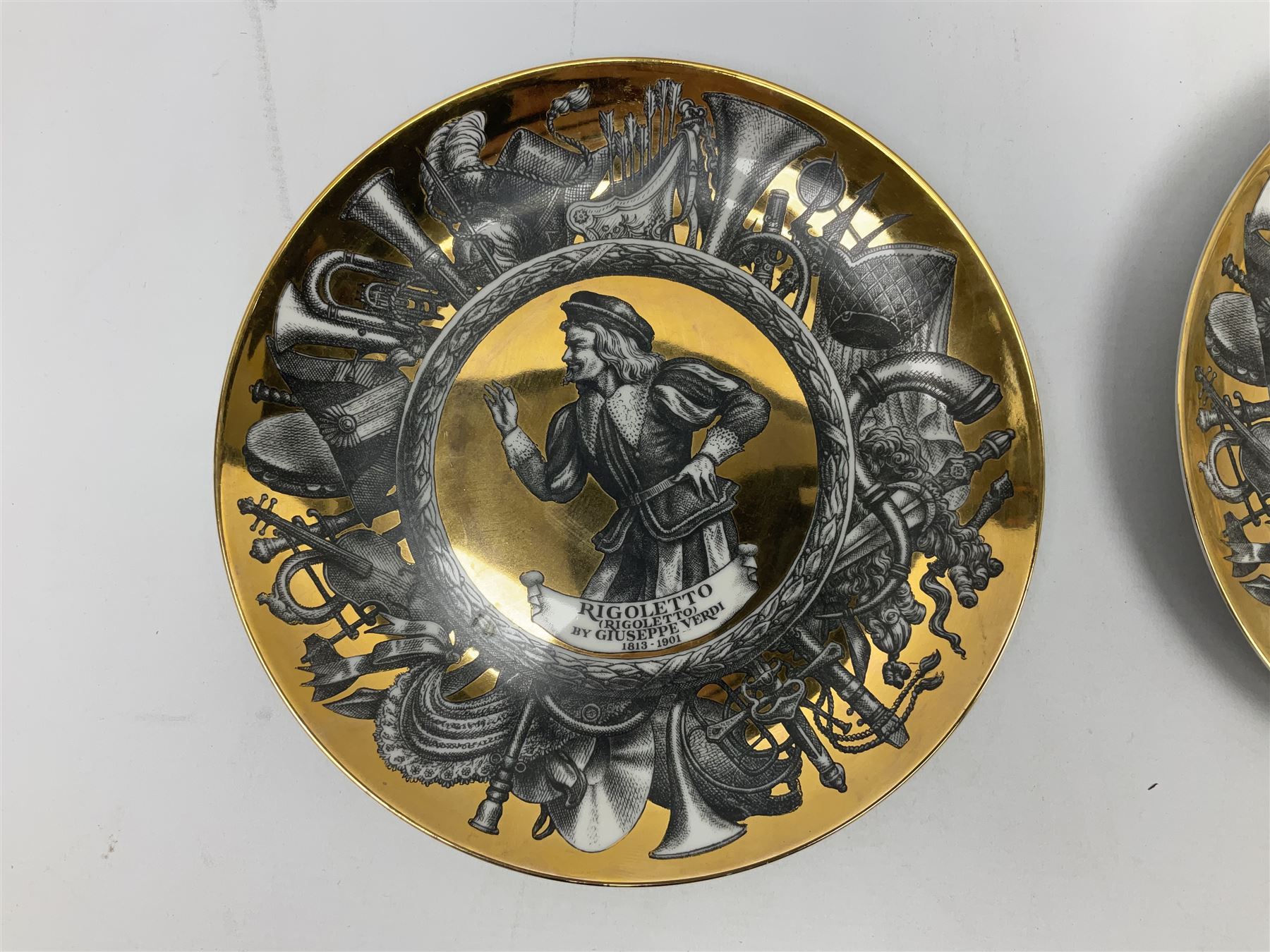 Three Fornasetti plates from the Melodramma series, each depicting a operatic portraits within a border of operatic emblems on gilt ground, with printed mark beneath, D25cm 