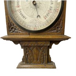 Edwardian - oak cased Arts and Crafts aneroid barometer with an 8” register, carved case with a flat top and dentil moulding, carved spandrels and carved plinth beneath, chrome bezel and flat bevelled glass (cracked)  steel indicating hand and brass recording hand, geometrically engraved dial centre, with an Arts & Crafts capitalized font, recording and indicating barometric pressure from 27 to 31 inches, with predictions.