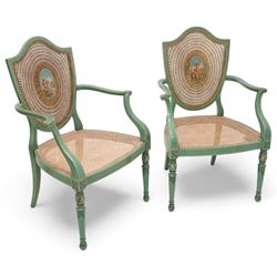 Pair of Edwardian Hepplewhite Revival green-painted open armchairs, cane work shield back with central oval panel panted with putto set upon rocky landscape with water and trees, shaped and rolled arms enclosing cane work seat, on turned front supports decorated with acanthus leaves and draped festoons 
