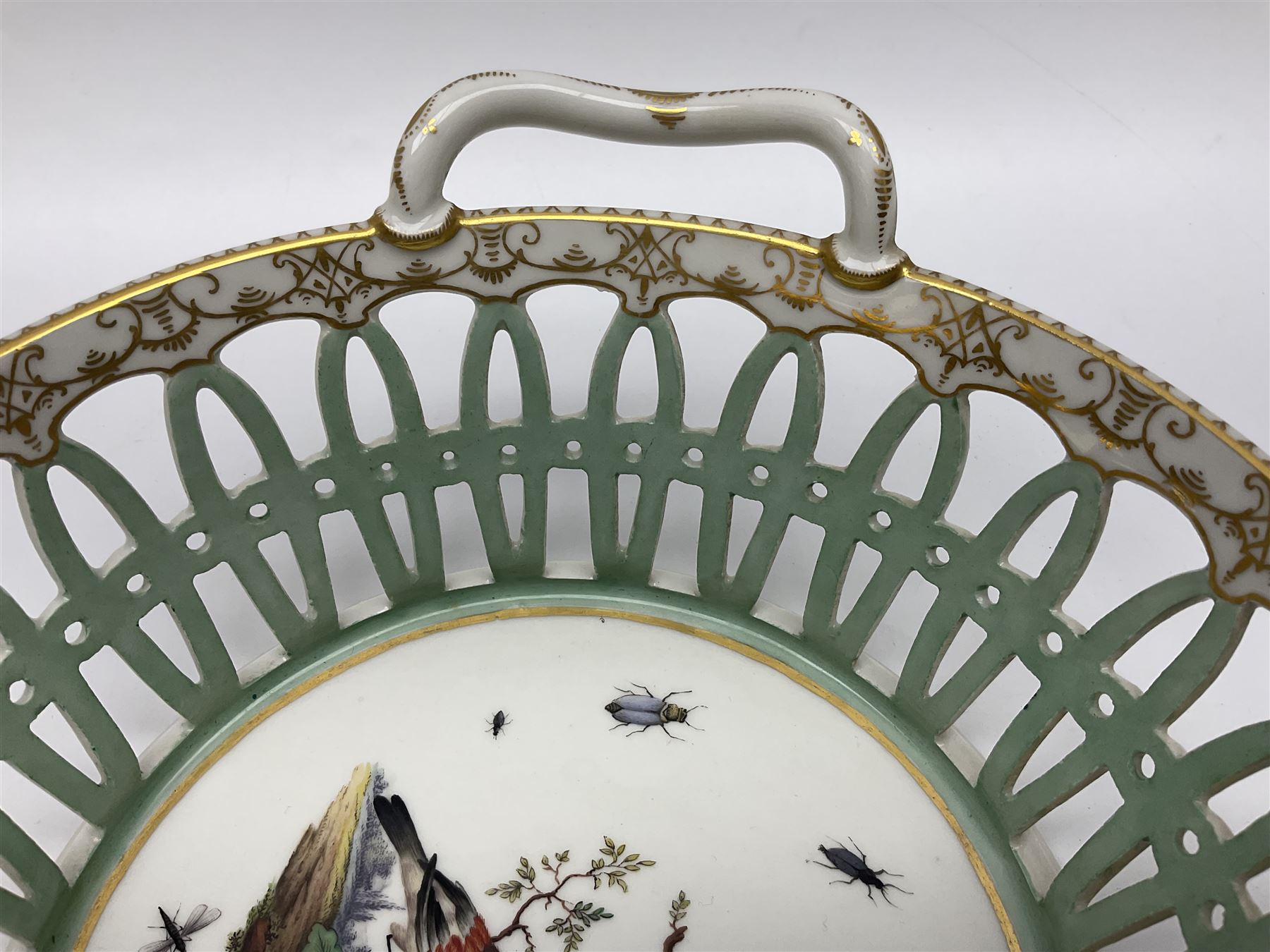 Pair of 19th century German openwork chestnut baskets, with twin handles and scrolling gilt border and star rim, painted to the centre with birds and insects, D22cm 