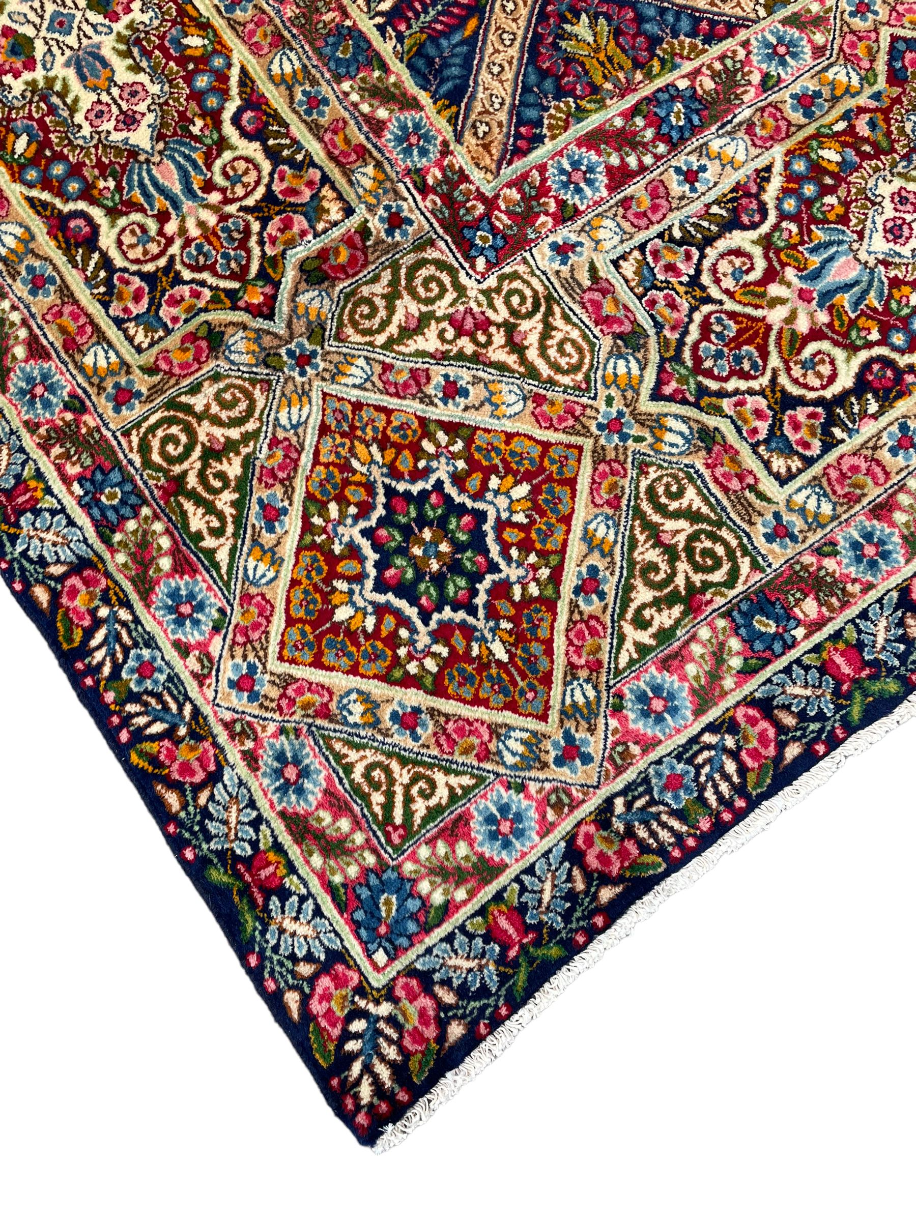 Persian Kirman indigo ground carpet, the field with repeating lozenge tiles with overall floral decoration, the main border with floral panels enclosed by the guards