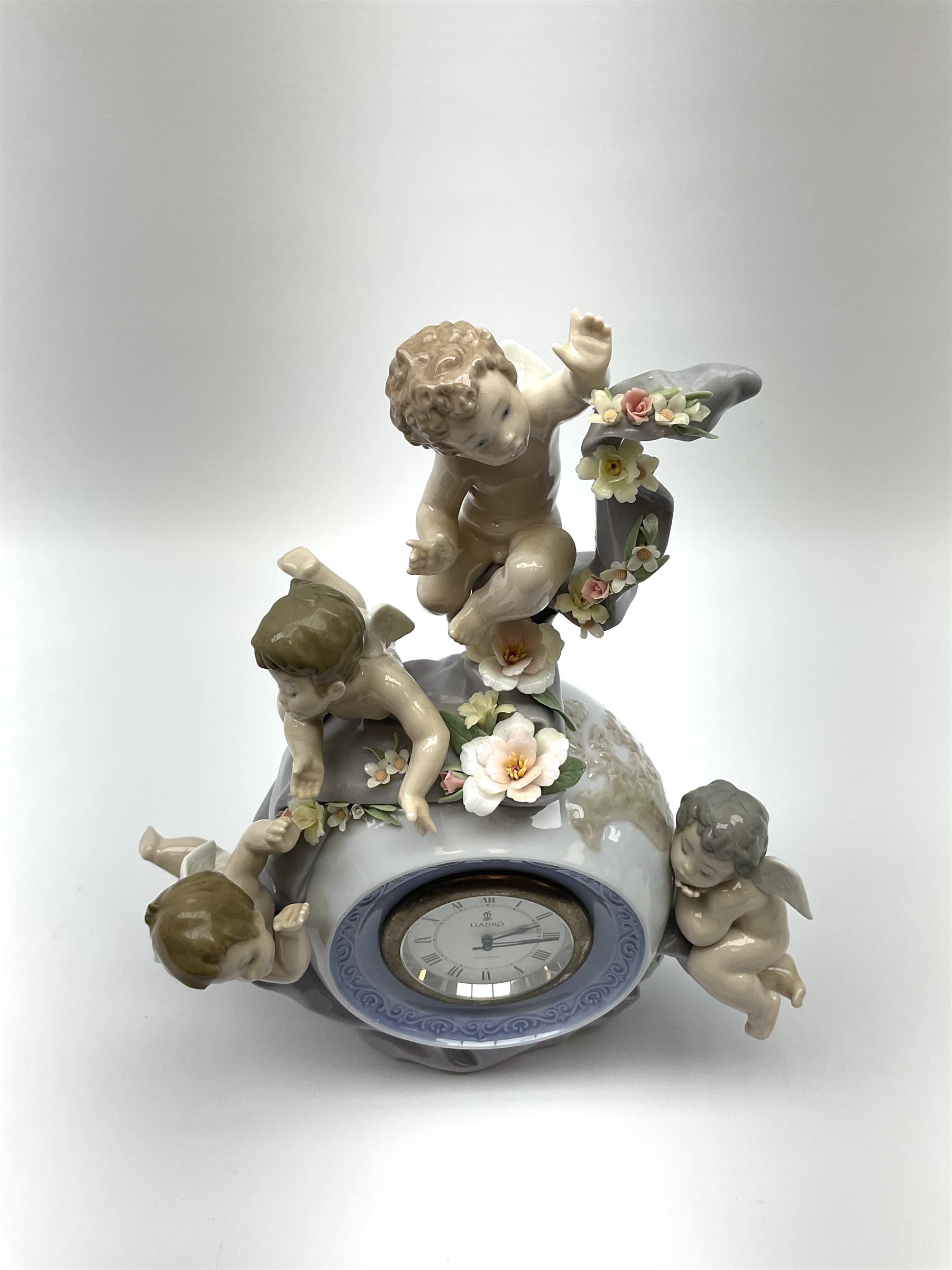 A Lladro mantel clock modelled as a globe with inset clock, surmounted by four putti and floral garlands, with blue printed mark and impressed 5973 beneath, H29cm.