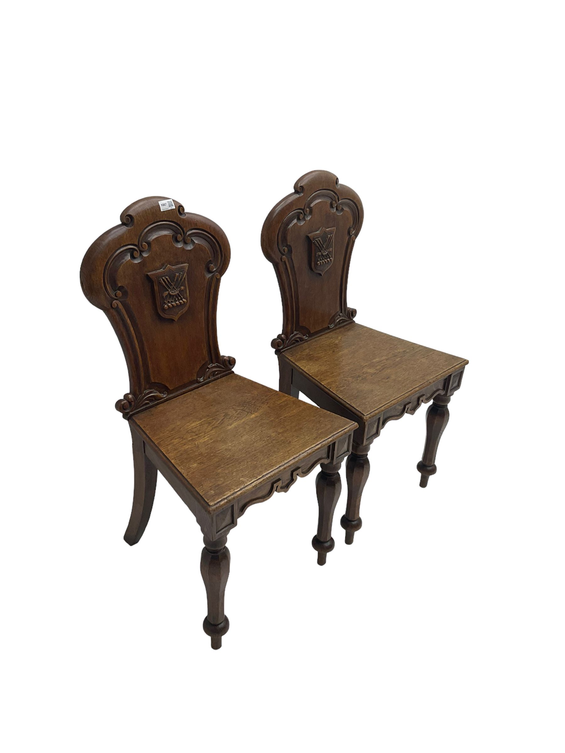Pair Victorian oak hall chairs, scallop shaped back with carved scrolls and central shield moulding, panel seat over shaped frieze rail, raised on turned supports