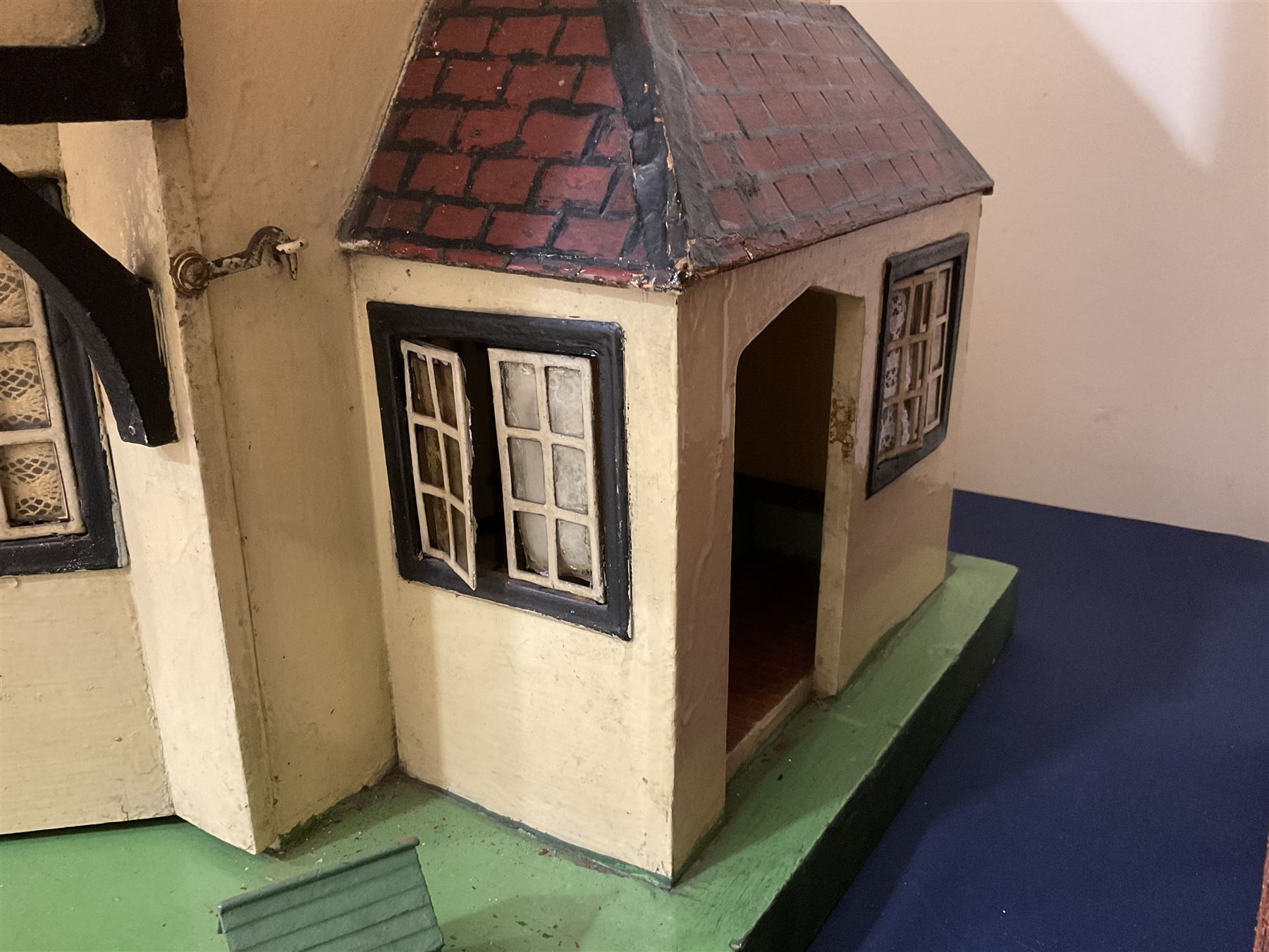 Large Tri-ang No.93 doll`s house in the 'Stockbroker's Range' c1935; two-storey double-fronted Tudor design, half timbered gables, two-storey bay windows, cream and mock shrubbery to front, opening metal framed windows with green shutters, red simulated tiled roof with chimney, integral garage with opening doors, front elevation has four hinged doors opening to reveal two bedrooms with fire places, living room, bathroom and kitchen with built in dresser and sink, entrance hall and staircase, side entrance with porch and seat and sun dial over on chimney stack; some wiring for electrical lighting; metal Tri-ang Toys disc verso; comprehensively furnished H66cm L117cm D43cm