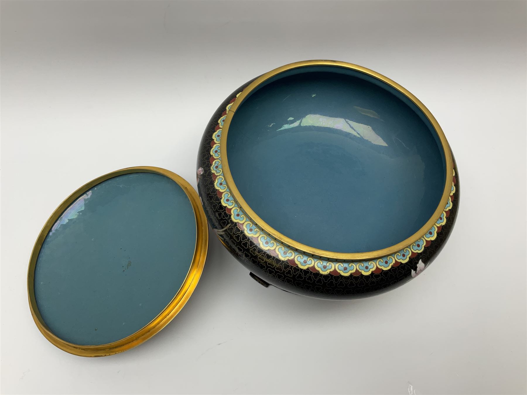 A Japanese cloisonne jar and cover, of squat form decorated with prunus blossom and birds in flight upon a black ground, with pierced wooden stand, jar D24cm.