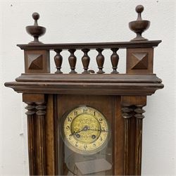 A German spring driven wall clock c1890, in a mahogany case with a glazed door, twin pilasters to the front and a balustrade gallery to the pediment, two-part dial with a repousse gilt centre and enamel chapter, Roman numerals and pierced steel hands, with an embossed gridiron pendulum and beat plate, eight-day spring driven movement striking the hours on a coiled gong.  With Key. 

