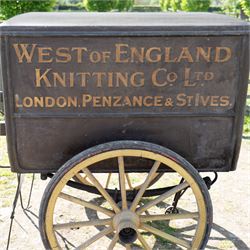 West of England Knitting Co. Ltd. Advertising Hand Cart

A rare and highly decorative late Victorian or Edwardian advertising hand cart, retaining its original black painted finish and gilt signwriting for West of England Knitting Co. Ltd., London, Penzance & St Ives. The enclosed box body is mounted on large cream painted wooden spoked wheels and fitted with rear push handles, allowing the cart to be manoeuvred by hand. Intended as a promotional and delivery vehicle for one of Britain's best known knitwear manufacturers, the cart survives as an evocative piece of commercial advertising history. The interior remains accessible via twin rear doors, while traces of the original maker's transfer for the Warwick Carrier are visible. An unusual and attractive display piece suited to collectors of advertising, transport memorabilia and social history.

Features

• Original hand painted gilt signwriting for West of England Knitting Co. Ltd.
• Advertising panels referencing London, Penzance and St Ives
• Enclosed wooden box body with twin rear access doors
• Original black painted finish with period lettering
• Large cream painted wooden spoked wheels with iron tyres
• Rear push handles for hand propelled operation
• Warwick Carrier maker's transfer remains visible
• Original undercarriage and running gear
• Attractive display piece with strong commercial advertising appeal
• Suitable for museum, retail, interior or collection display

Dimensions:
Overall length: 190 cm
Body length: 125 cm
Overall width: 140 cm
Body width: 100 cm
Height: 150 cm

Wheel Diameter:
Wheels: 92 cm