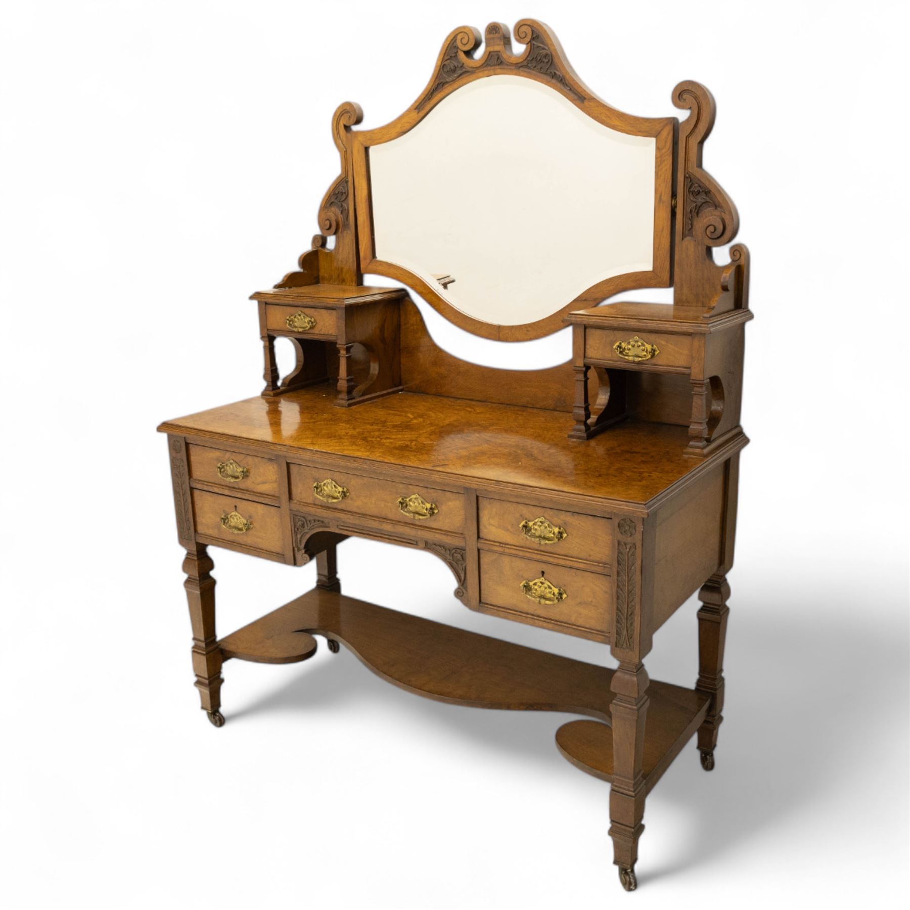 Late Victorian burr walnut veneer dressing table, the arched swing mirror surmounted by pierced scroll cresting, flanked by twin drawers on turned columns, over moulded rectangular top with five drawer arrangement, on block supports with shaped undertier