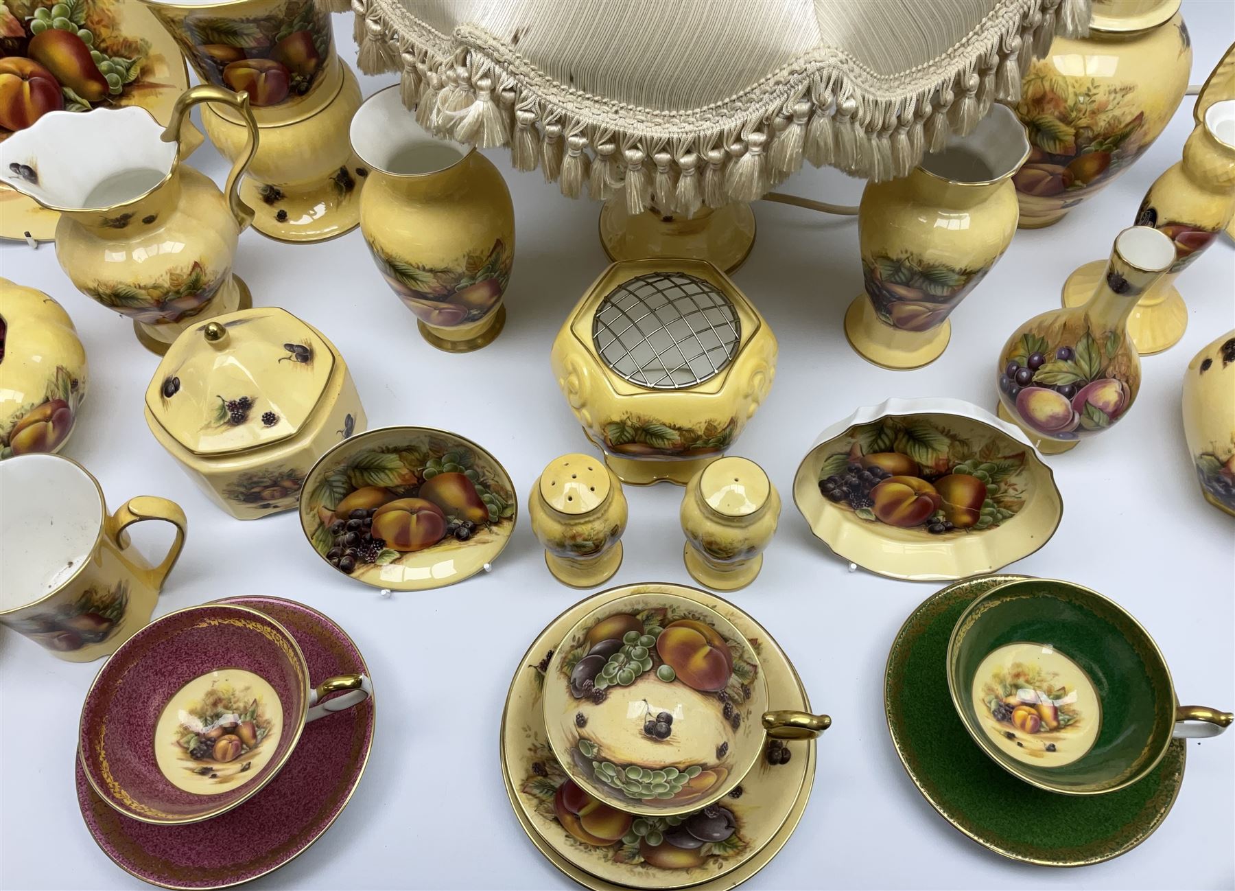 Collection of Aynsley Orchard Gold pattern wares, comprising lamp base, three jars and covers, six vases or various size and form, large jug, lidded dish, pair of cruets, pair of candlesticks, mug, two pin dishes, lobed dish, tea cup, saucer, size plate, and cake plate, and two further cups and saucers, each cup decorated with central Orchard Gold reserve to the interior against a mottled pink or green ground. 