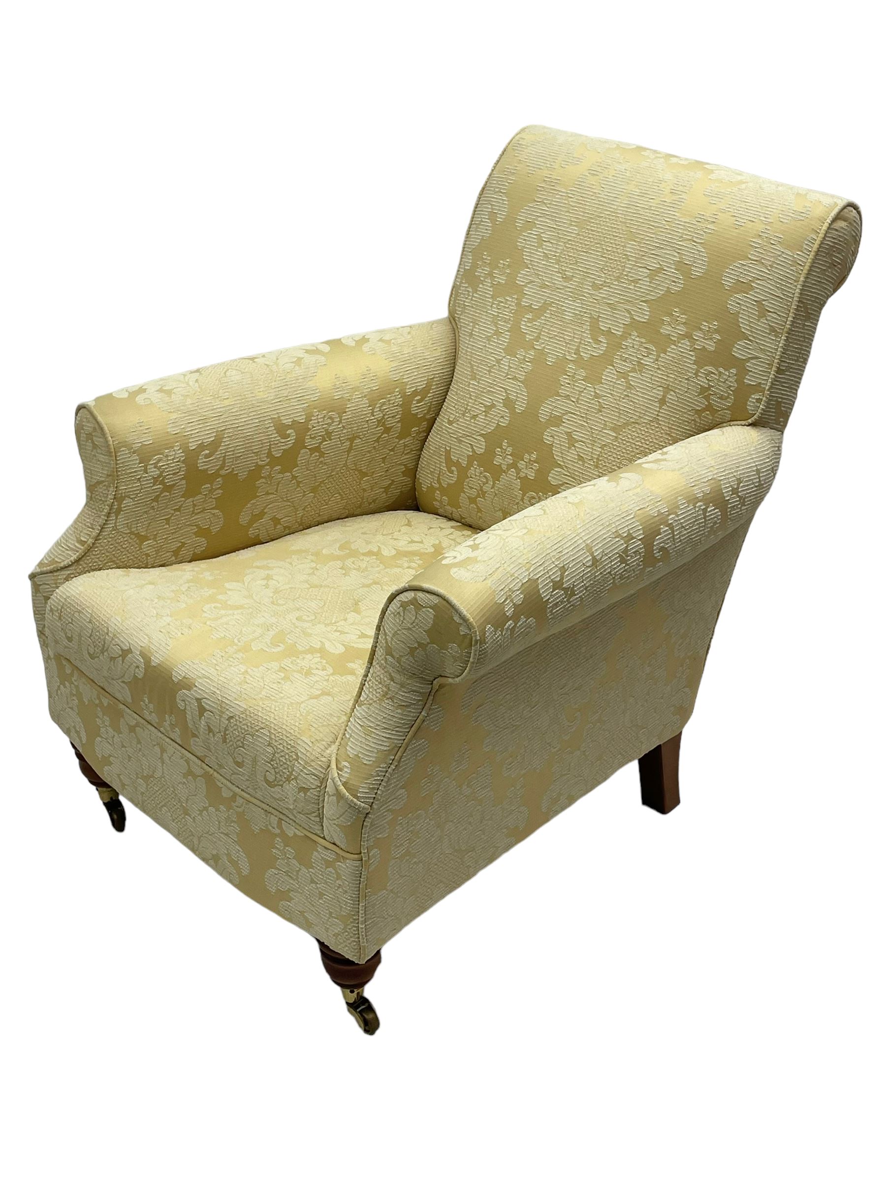 Traditionally shaped hardwood-framed armchair, rolled back and arms, upholstered in pale gold and cream damask fabric with repeating foliate pattern, on turned feet with brass cups and castors