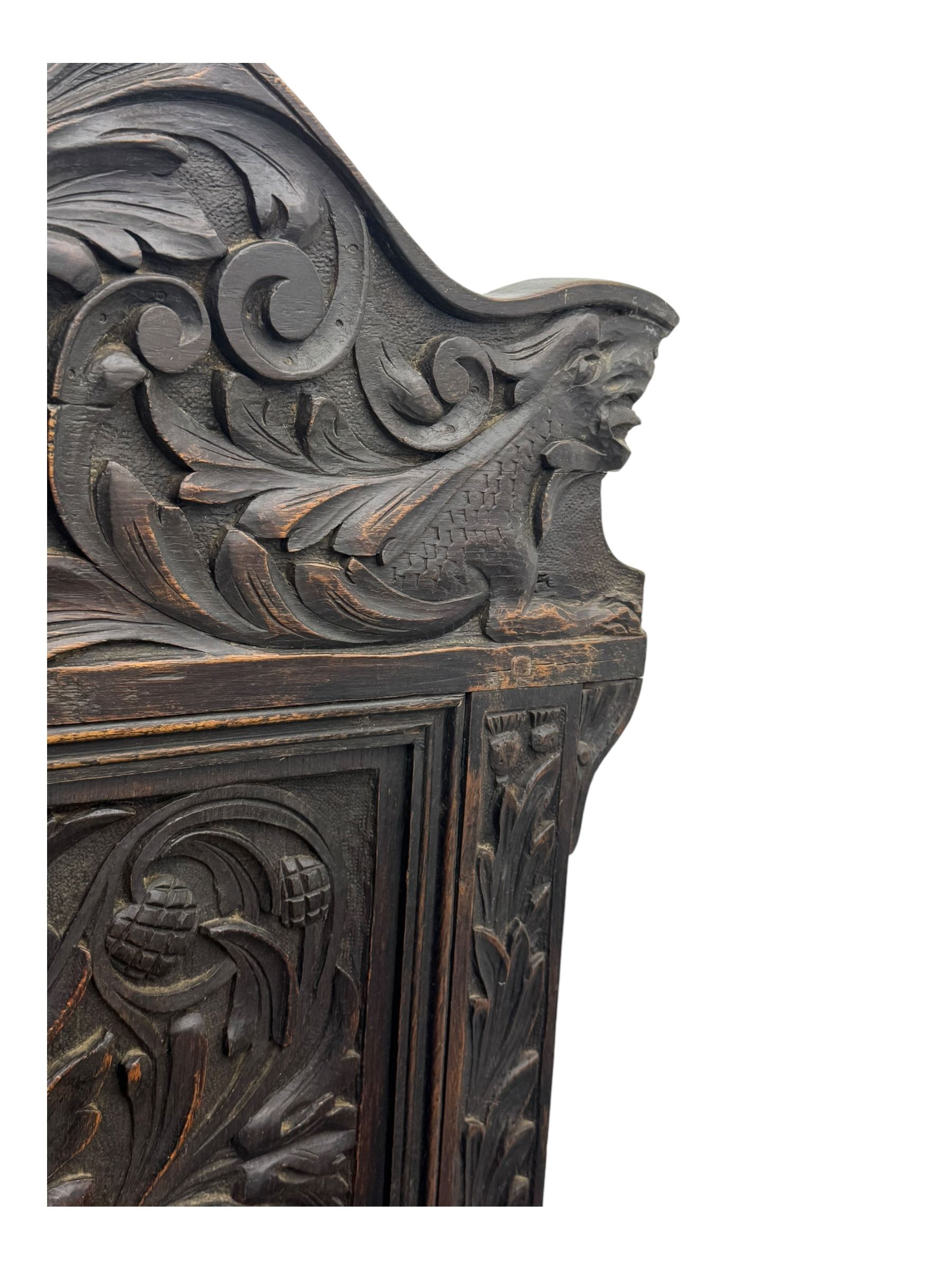 Late 19th century Jacobean revival carved oak armchair, the tall back with arched cresting featuring a stylised foliate mask, flanked by carved scrolls, relief carved panel depicting symmetrical foliage, downscrolled arms, on turned front supports united by stretchers