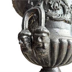 Pair of Victorian cast iron campana form garden urns, the gadrooned flared edge over a scrolling acanthus relief body, with twin male mask handles to each side, over a lobed underbelly with fluted socle, the rectangular pedestals with relief floral garlands and stepped base, in rustic black-painted finish, planted