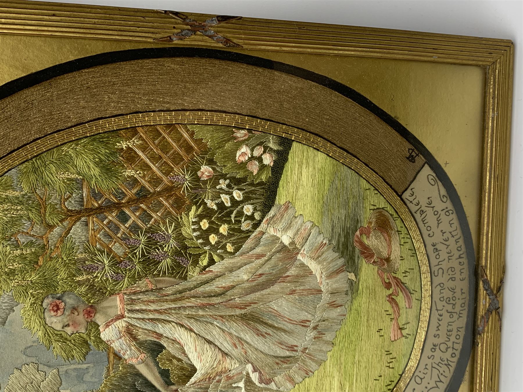 George III silkwork picture, of oval form depicting a female figure in garden setting, within a silkwork border detailed with verse from Robert Burns Bonnie Peg, 'Her air sae sweet, and shape complete, The Queen of Love did never move, Wi' Motion mair enchanting!', and monograms 'FV' and 'SM', in reeded gilt frame and gilt mount, indistinctly inscribed in pencil verso, overall H36cm L30.5cm