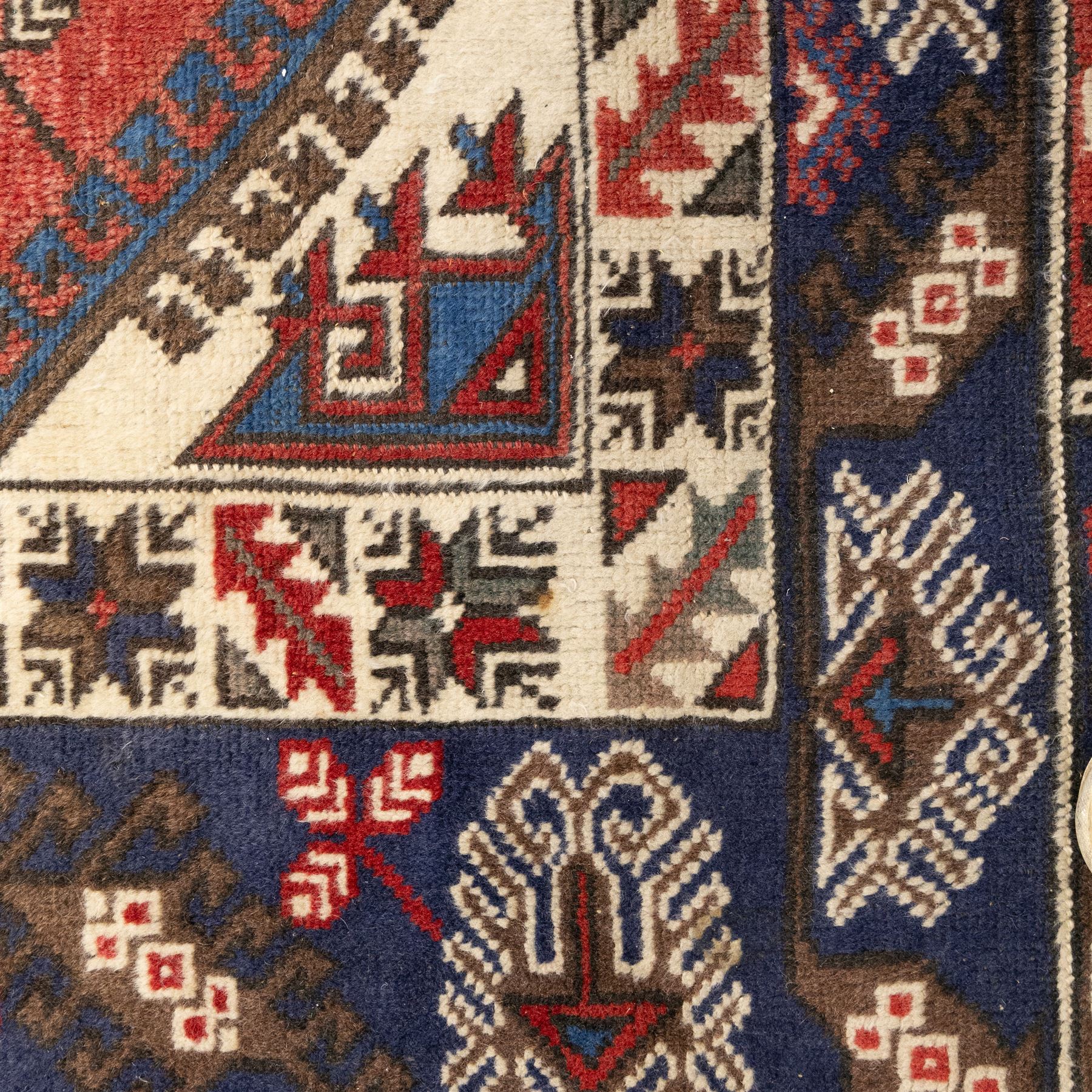 Caucasian Shirvan hand-knotted rug, red madder field with hooked lozenge medallions and stylized motifs, framed by ivory stepped spandrels and multiple geometric borders in indigo brown and ivory, with serrated palmettes and angular devices 