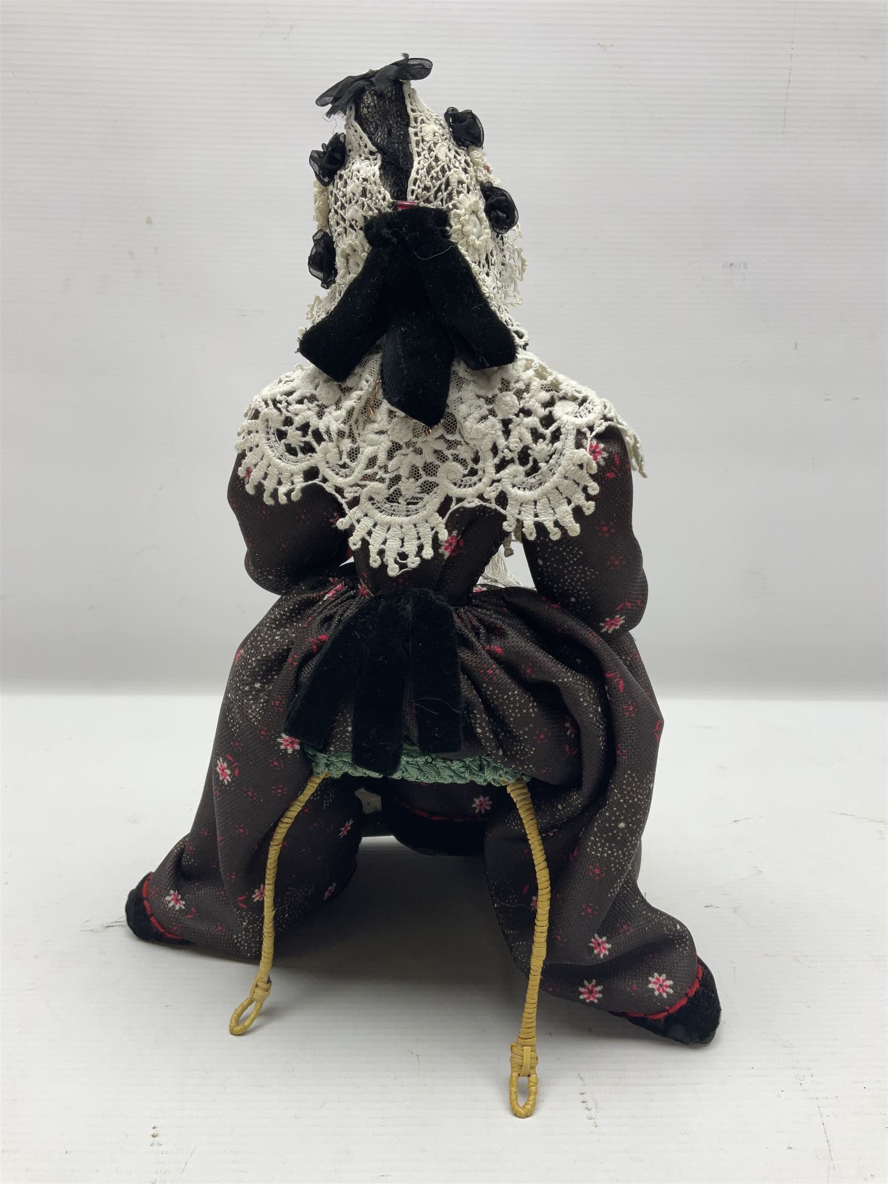 Anna Meszaros Hungary - hand made needlework figurine 'Old Lady' seated on a stool wearing a lace trimmed black/white/red floral full length dress and hat, working on a piece of lace H30cm  Auctioneer's Note: Anna Meszaros came to England from her native Hungary in 1959 to marry an English businessman she met while demonstrating her art at the 1958 Brussels Exhibition. Shortly before she left for England she was awarded the title of Folk Artist Master by the Hungarian Government. Anna was a gifted painter of mainly portraits and sculptress before starting to make her figurines which are completely hand made and unique, each with a character and expression of its own. The hands, feet and face are sculptured by layering the material and pulling the features into place with needle and thread. She died in Hull in 1998.