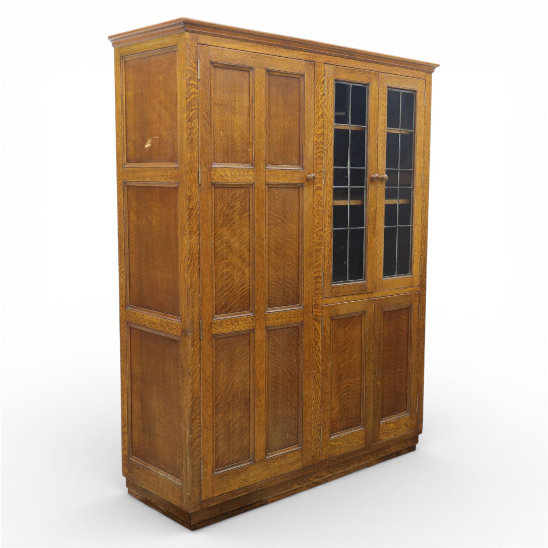 Edwardian oak glazed cabinet, moulded cornice above a panelled front and sides, fitted with lead glazed doors enclosing shelved interior, left side full length cupboard converted to enclose a gun cabinet, on a plain plinth base 