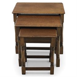 Nest of three dark oak tables, rectangular top with turned supports, tables suspended on rails