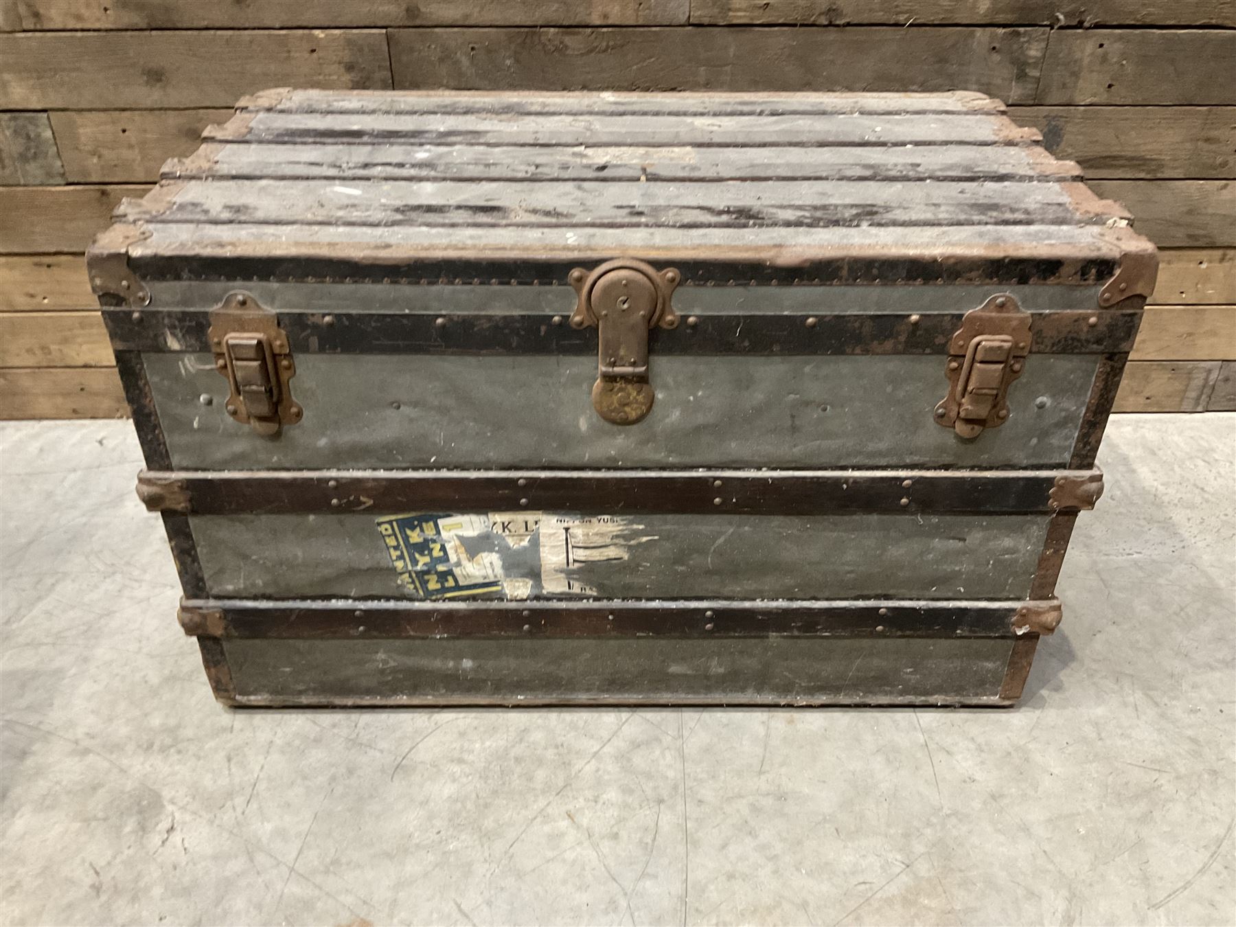 Early 20th century wood and metal bound zinc travelling trunk, hinged top with three clasps, decorated with period luggage labels