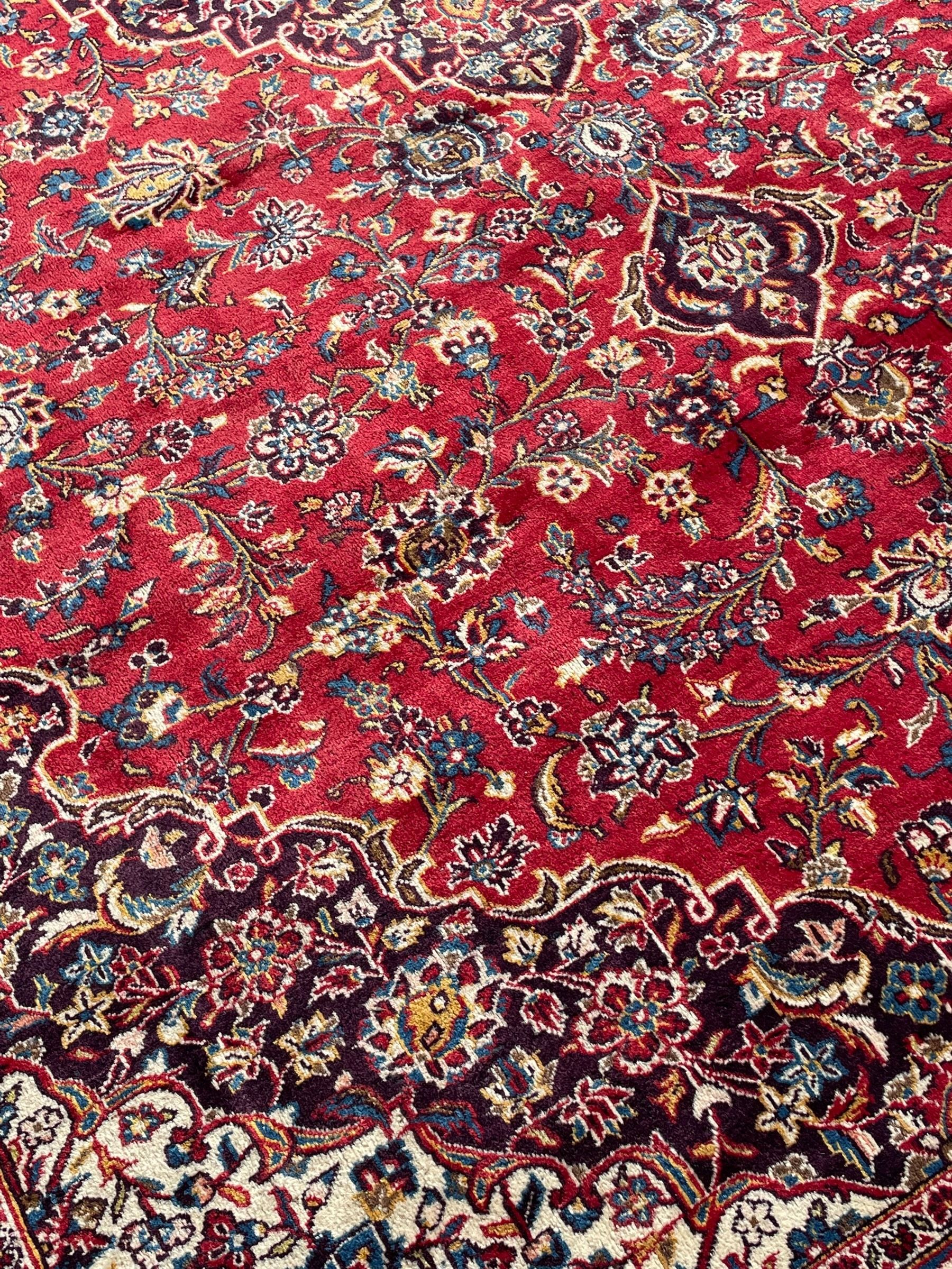 Large Persian Kashan crimson ground carpet, large floral central medallion surrounded by trailing branches decorated with leaves and stylised plant motifs, the main border with scrolling design interspersed with palmettes, within floral pattern guard stripes 