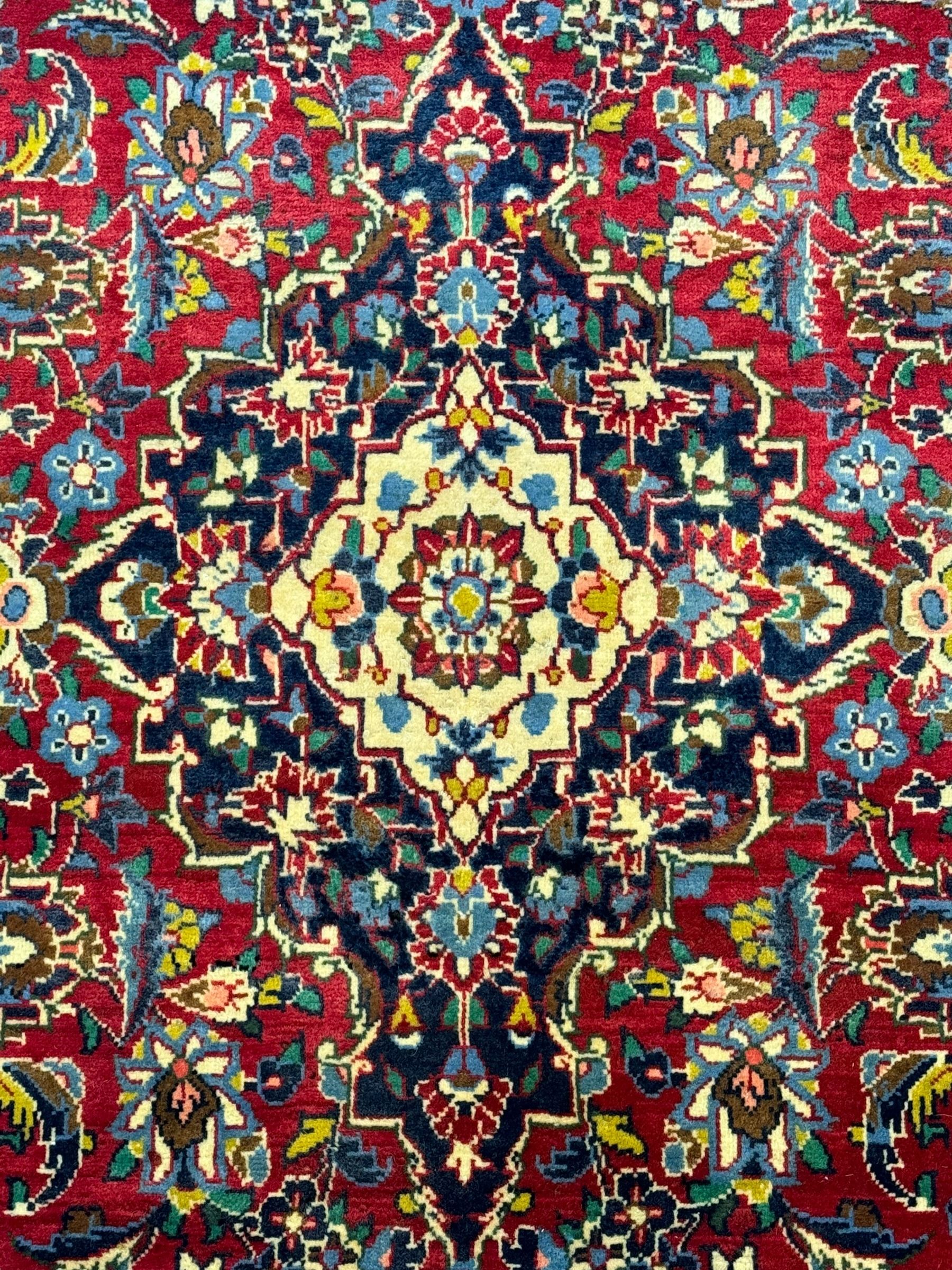 Central Persian Kashan crimson ground rug, central indigo pole medallion surrounded by sparsely placed bouquets interconnected with foliate branches, the guarded border with repeating palmette and Boteh motifs with interwoven scrolling patterns, framed by guard stripes