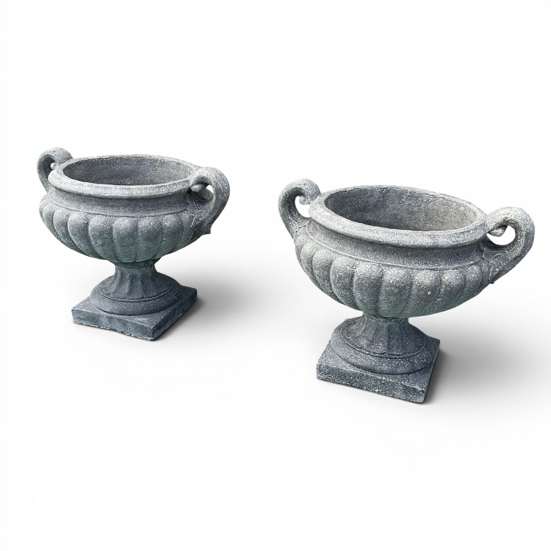 Pair of squat cast stone garden urns of kylix form, gadrooned body with twin pierced scrolling handles, fluted socle on square base