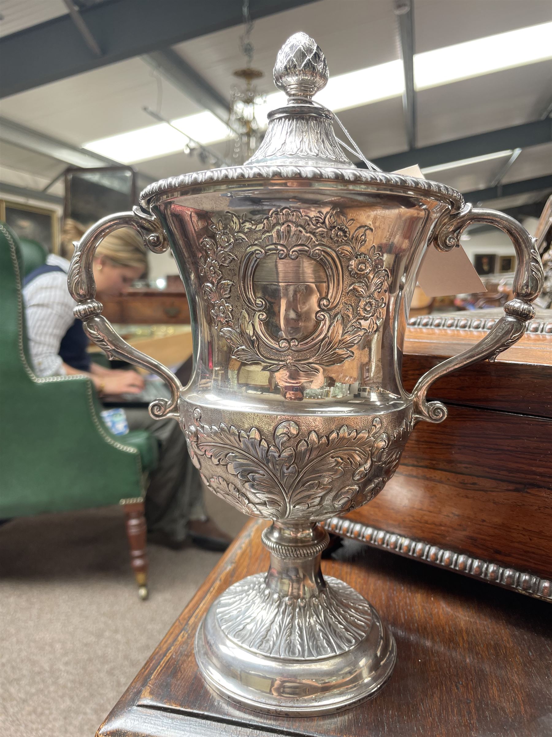 George III silver two handled campana shape cup and cover with pineapple lift, the body with cartouche surrounded by flowers above leaves and scrolls on a pedestal foot with acanthus leaf decoration H29cm London 1764, makers marks rubbed