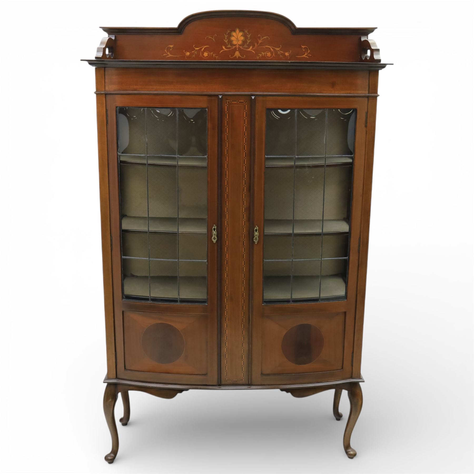 Edwardian mahogany display cabinet, arched back with satinwood and harewood marquetry foliate decoration above a moulded cornice, serpentine front fitted with twin glazed doors with astragal bars, the lower door panels inlaid with oval reserves, standing on elegant cabriole legs terminating in pad feet