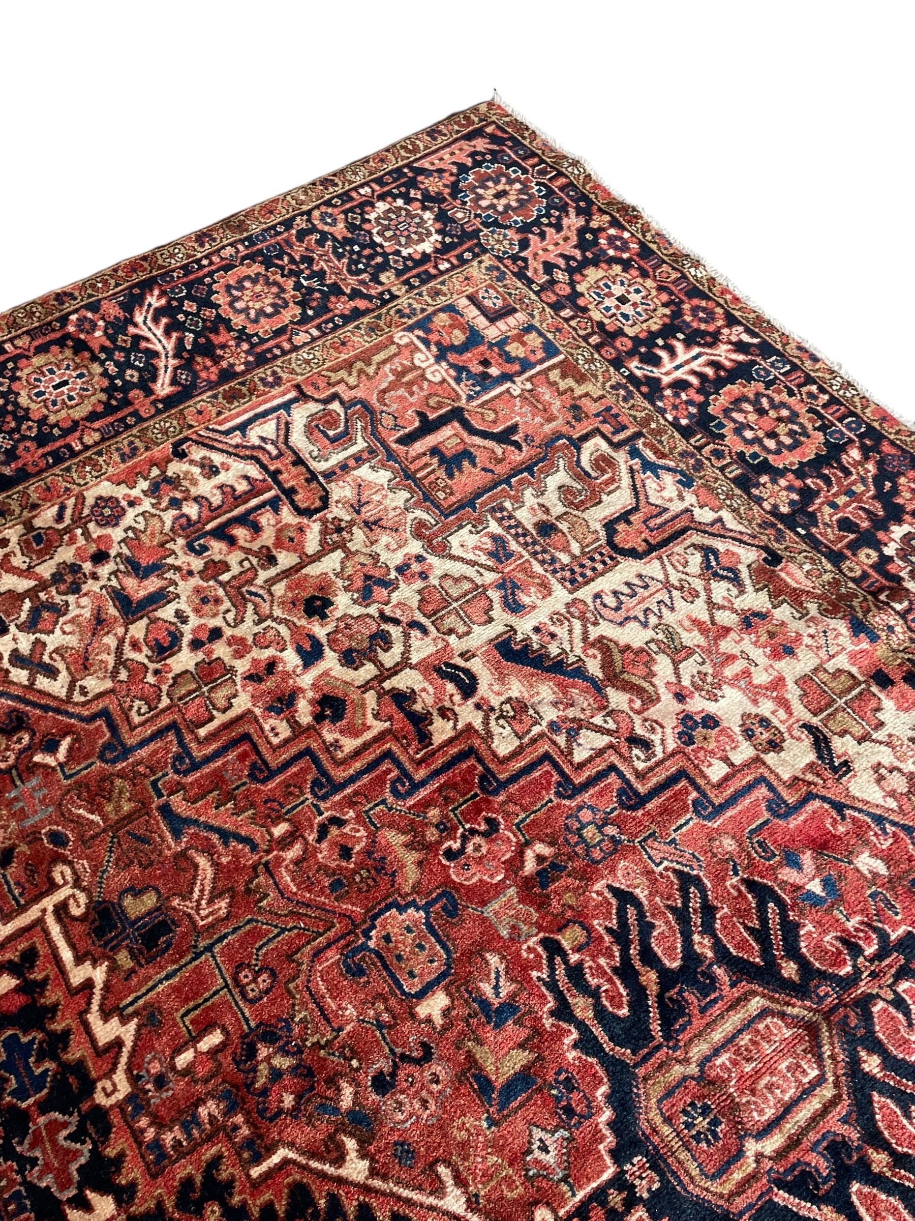 Persian Heriz red ground carpet, large stylised pole medallion surrounded by Pitrak motifs, indigo ground border decorated with stylised flower heads and trailing leafy branches, within floral pattern guard stripes