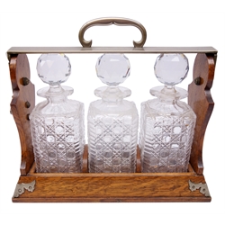  Edwardian Betjemann's three division tantalus, oak frame with EPNS mounts, stamped Patent 26435, the three hobnail cut glass decanters with prismatic cut stoppers, W37cm x H33cm   