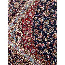 Persian Kashan indigo ground carpet, central floral pattern medallion surrounded by a densely decorated field depicting trailing branches with leaves and palmettes, scrolling border decorated with stylised plant motifs, within floral pattern guard stripes 