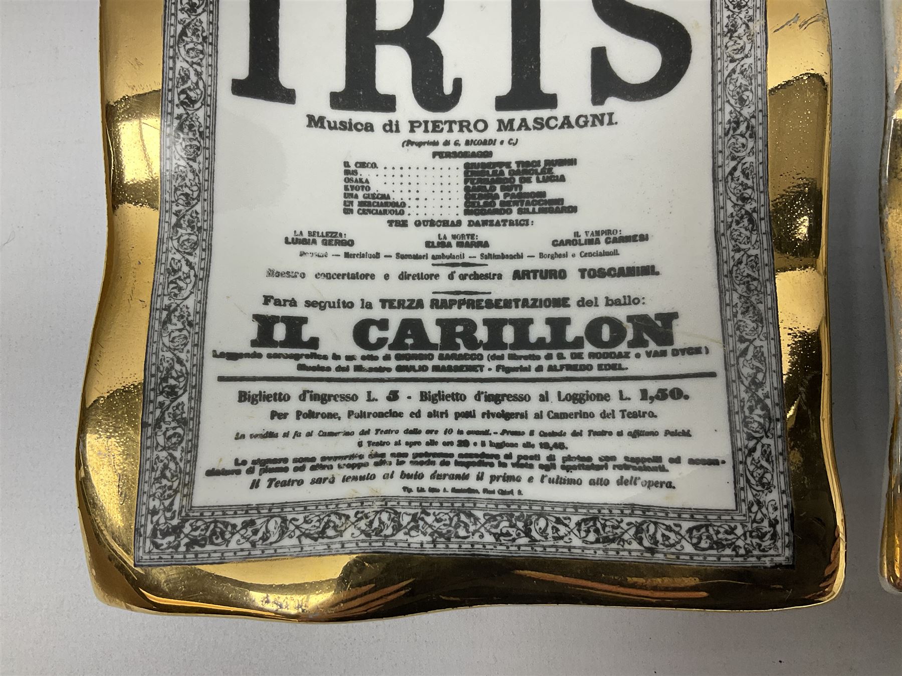 Two Fornasetti rectangular operatic posters ashtrays 'Norma' and 'Iris' decorated with black and white text with a gilt border edge, with printed mark beneath, H16cm