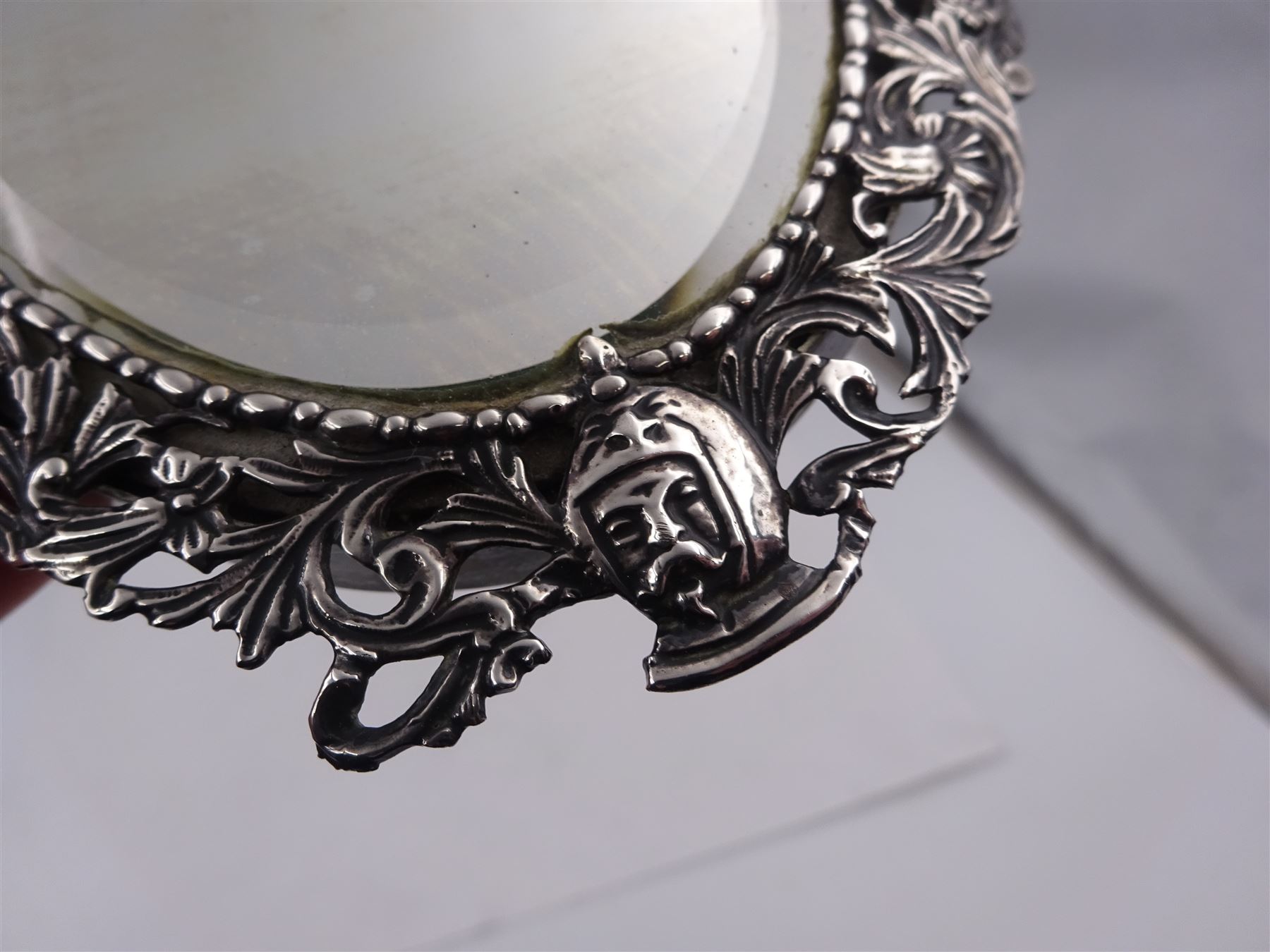 Continental silver miniature dressing table/wall mirror, of oval form with bevelled mirror plate, surrounded by a bead and dart rim, with pierced scrolling floral border with a standing cavalier to either side and the bust of a cavalier to the base, H17.7cm