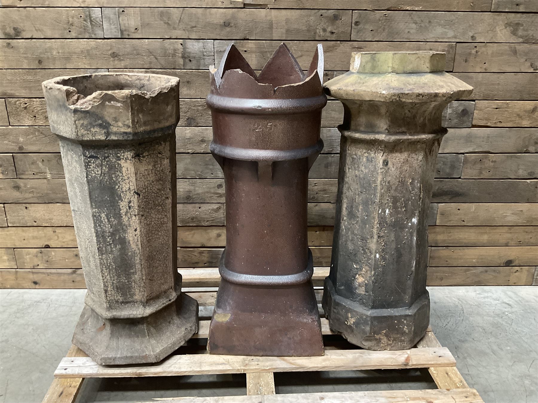 Collection of three Victorian and early 20th century reclaimed terracotta chimney pots, comprising: one cylindrical form with weathered, cracked glaze and flared octagonal base; one deep red cylindrical pot with fluted midsection and castellated rim, bearing moulded number ‘25’; and one tapering hexagonal example with wide flared rim and weathered patina. All with age-related wear and chips, consistent with use and outdoor exposure. Plus a selection of cast stone pieces including fountain 