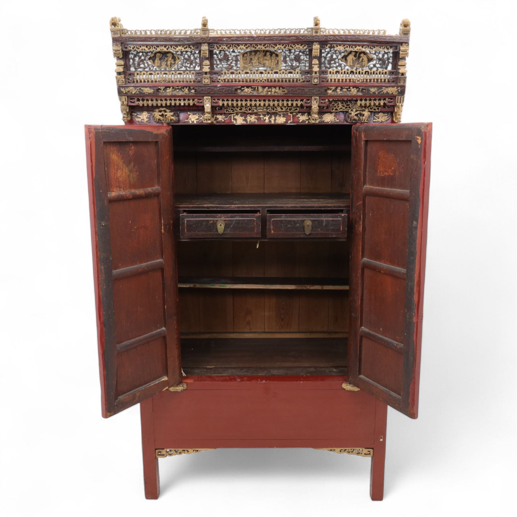 Early 20th century Chinese lacquered marriage cabinet, of rectangular form in red lacquer, fitted with double doors centred by circular brass lock plate and drop handles, the interior with shelves and two short drawers, cornice and apron with giltwood foliate and figural carving, together with an elaborately pierced and gilded wooden cresting panel carved with scenes of figures within pavilions and stylised dragons