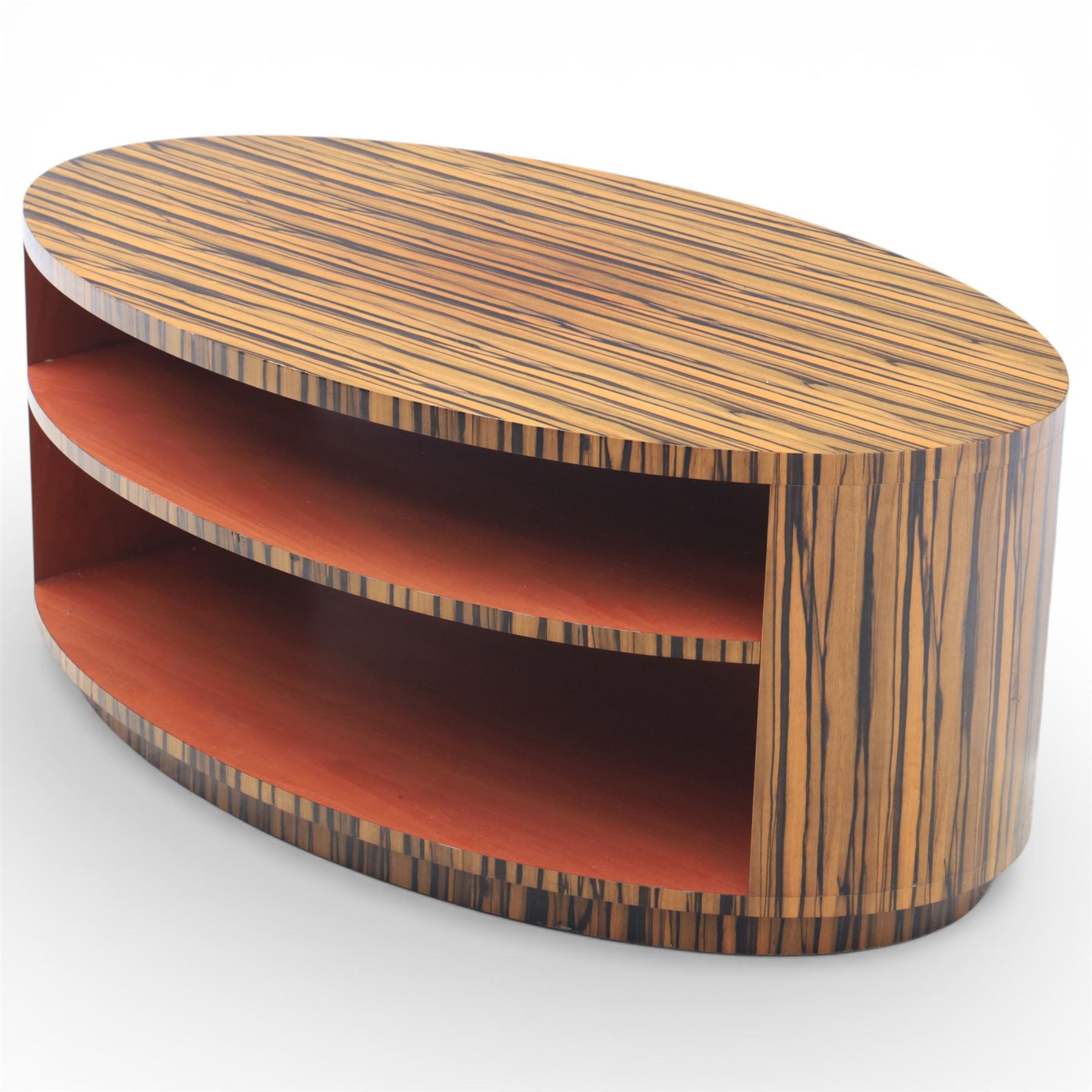 Toby Winteringham - Mid 20th century zebra wood coffee table, oval top with book matched striped veneers over two open tiers painted red, the curved end supports and continuous plinth base veneered to match, recessed plinth base 