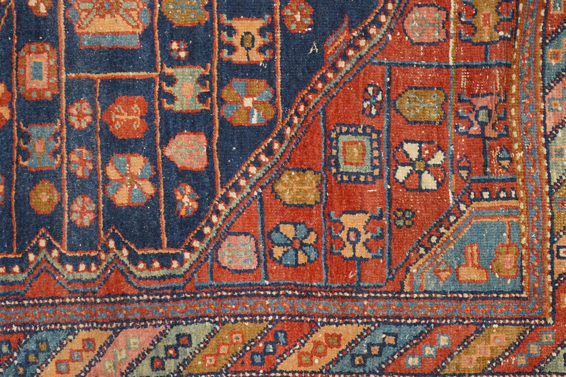 Persian Heriz hand-knotted carpet, terracotta ground centred by large dark navy geometric medallion with stepped outline, decorated throughout with stylised flowerheads, palmettes and geometric motifs in blue, green and ochre, enclosed by diagonal geometric border with narrow guard stripes