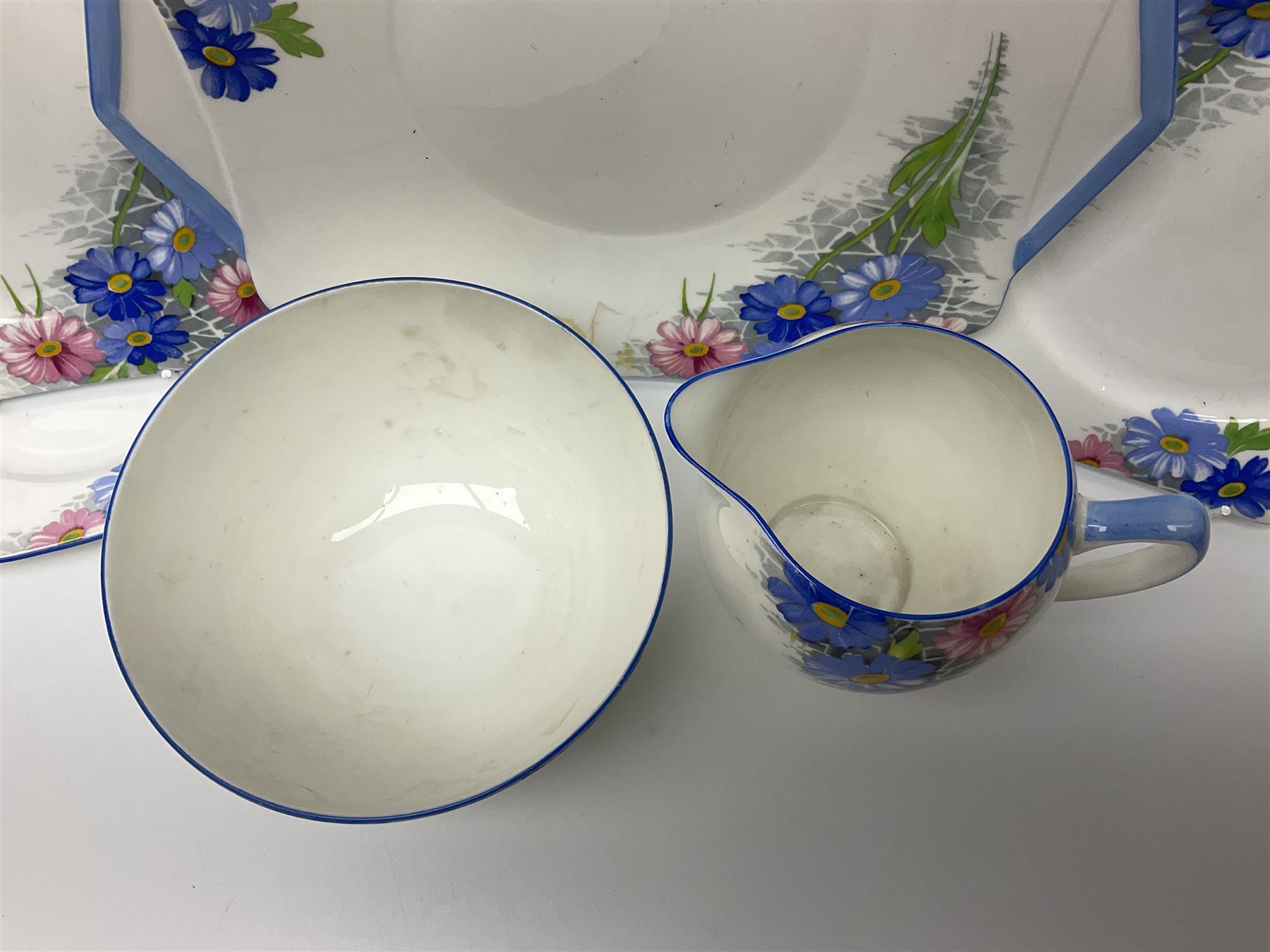 Shelley Strand shaped tea wares, decorated with blue and pink daisies upon a white ground, comprising four teacups, four saucers, three tea plates, milk jug, sugar bowl and cake plate, all with printed green mark beneath and painted pattern no 12216