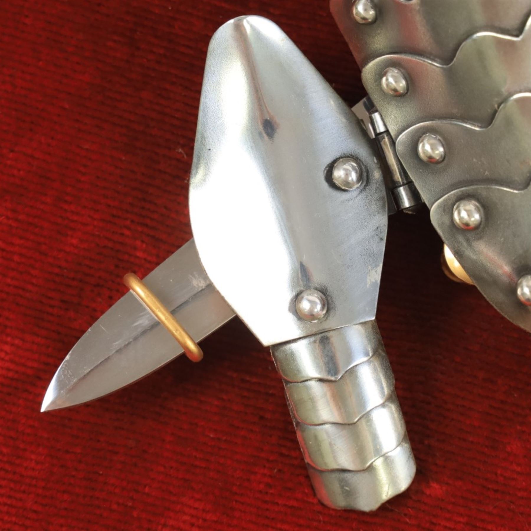 Three replica gauntlets, each housed upon a red wall shield, two with daggers, the third with a sword, largest H102cm