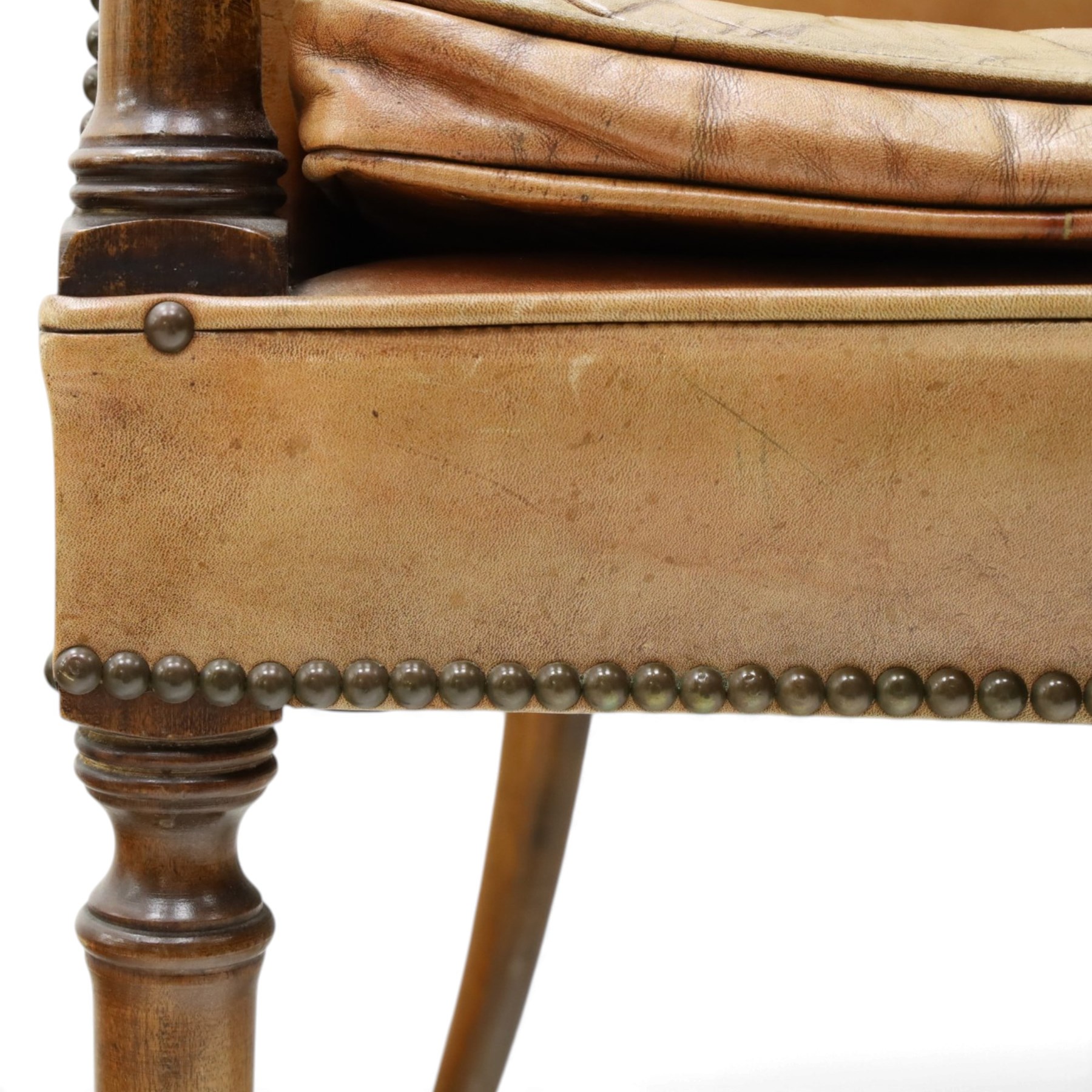 Early 20th century Georgian design mahogany framed desk or club armchair of tub form, with turned pilaster arm supports and legs with rear splayed supports, upholstered in faded tanned leather with loose seat cushion