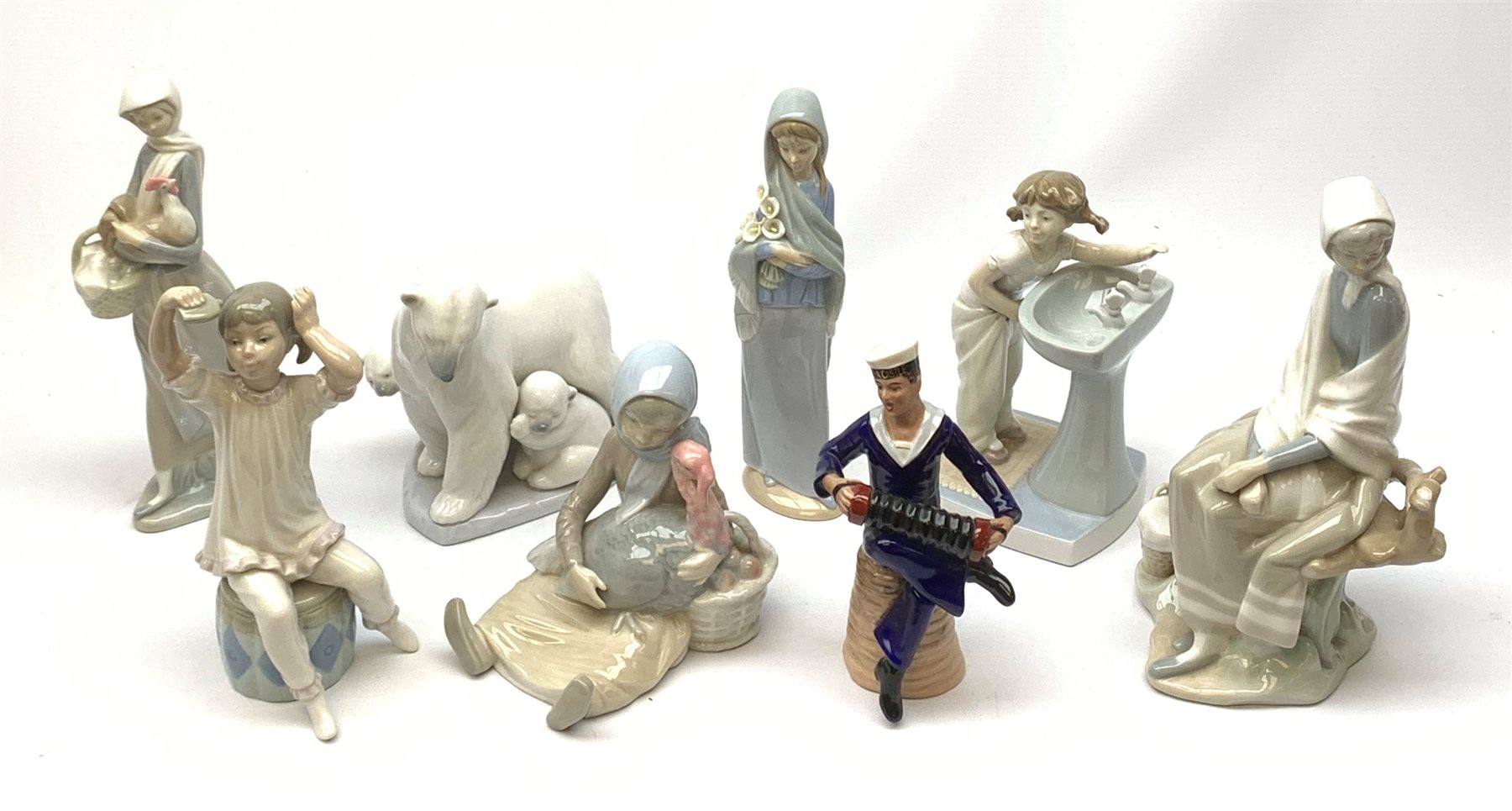 A mid 20th century Dresden porcelain figurine, modelled as a sailor playing an accordion, H16.5cm, together with a collection of seven Lladro figurines, to include a polar bear figure group. 