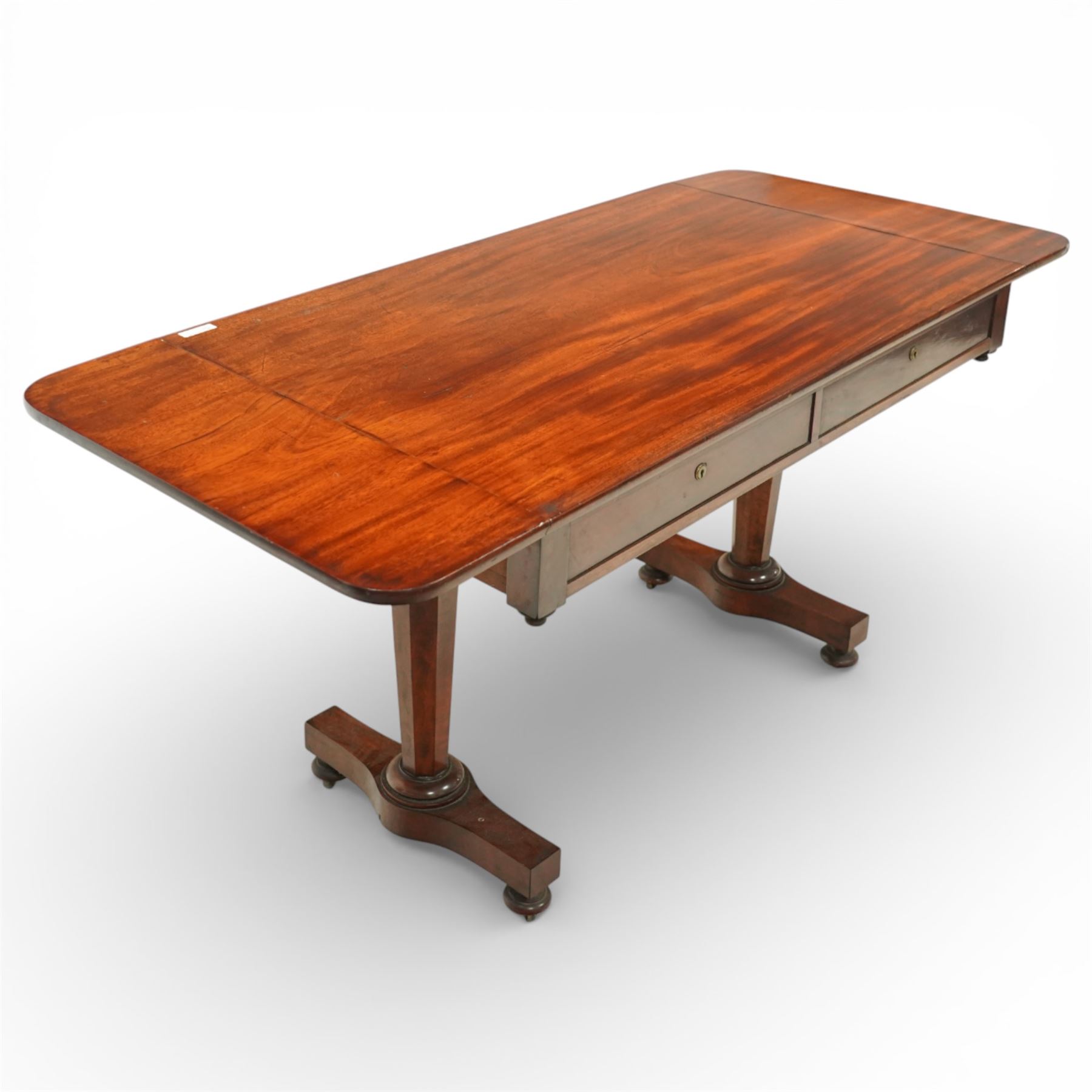 William IV mahogany sofa table, the rectangular top with rounded corners and hinged drop leaves to either end, above a shallow frieze fitted with two drawers opposing conforming dummy drawers, supported on octagonal tapering legs with ring turnings, joined by a shaped stretcher and raised on platform bases with scroll feet