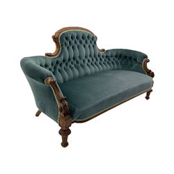 Victorian walnut framed settee, the raised arched back carved with foliate, buttoned back upholstered in blue fabric, c-scroll carved arms supports carved with bell flowers, turned front feet with carved and fluted decoration 