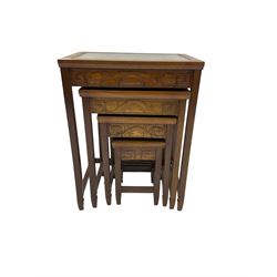 Mid-20th century nest of four Singapore hardwood tables, glass topped insets carved with traditional scenes of figures, carved frieze with landscape design on square tapering supports