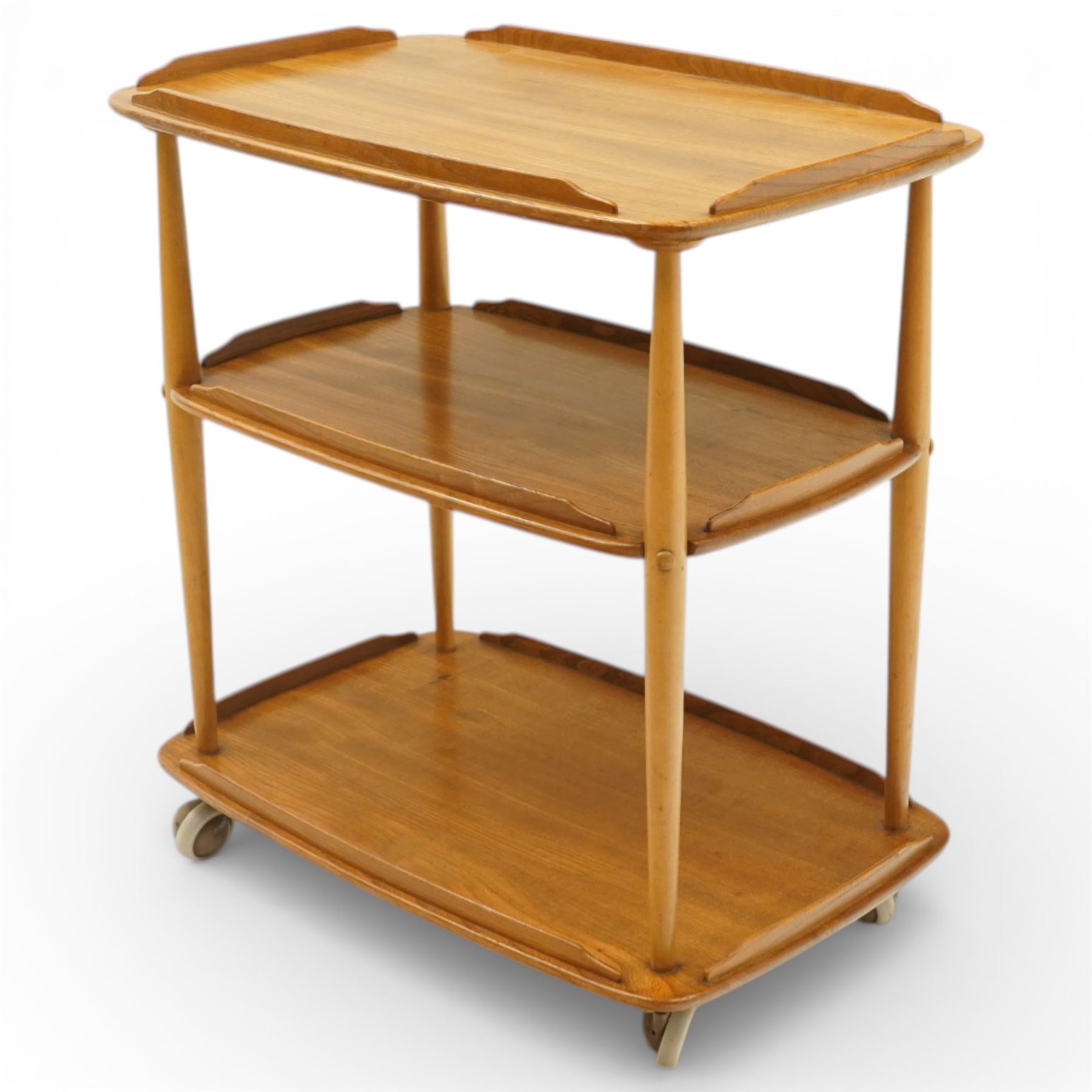 Ercol - elm tea trolley, Model 458. Rectangular three-tier form with shaped gallery edges, supported on turned upright supports, raised on castors
