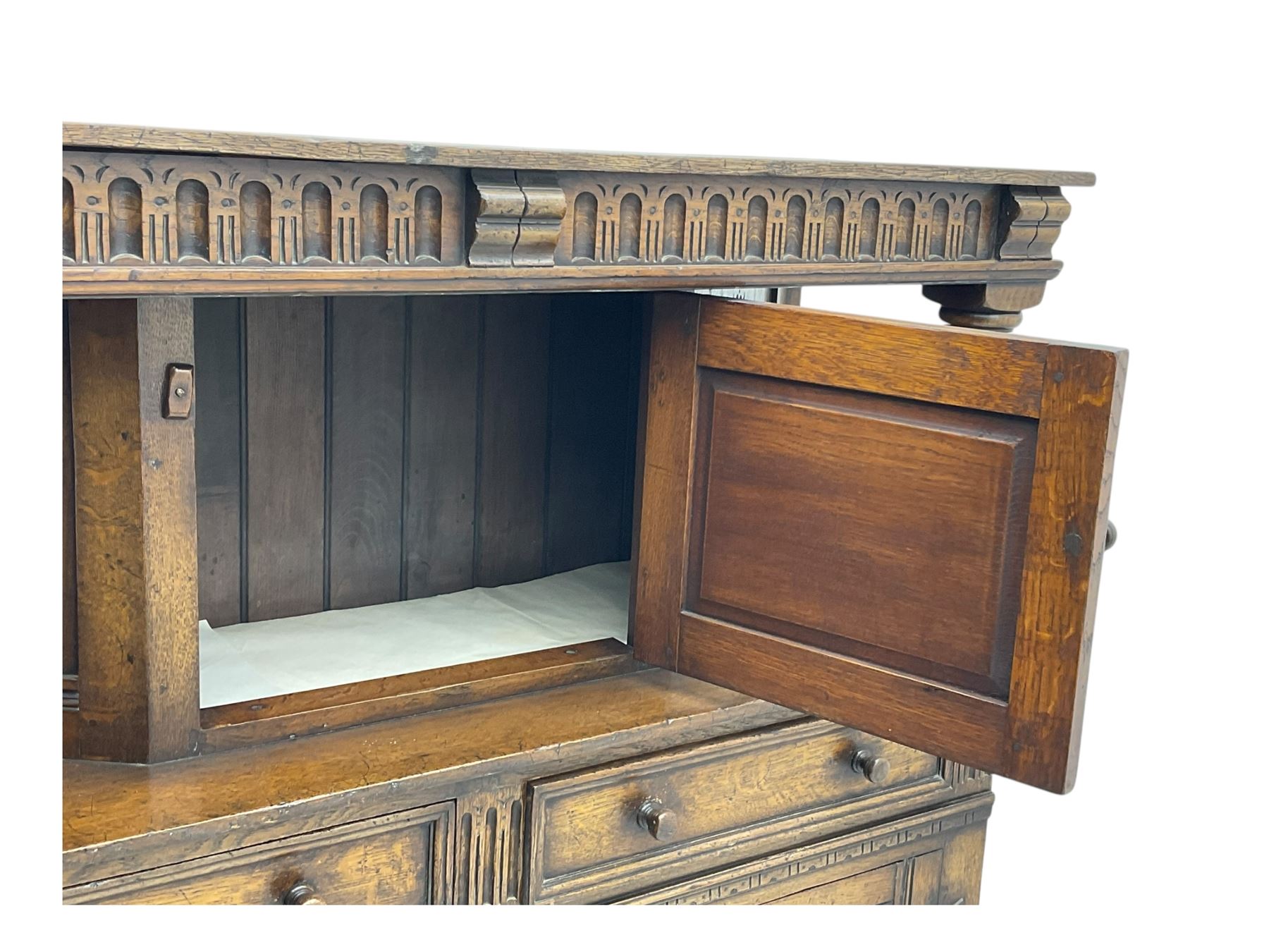 Jacobean design oak court cupboard, upper section with carved arched panelled cupboard door flanked by turned columns, beneath carved and moulded frieze, lower section fitted with two drawers over two cupboard doors with gothic arched panel decoration, raised on stile supports