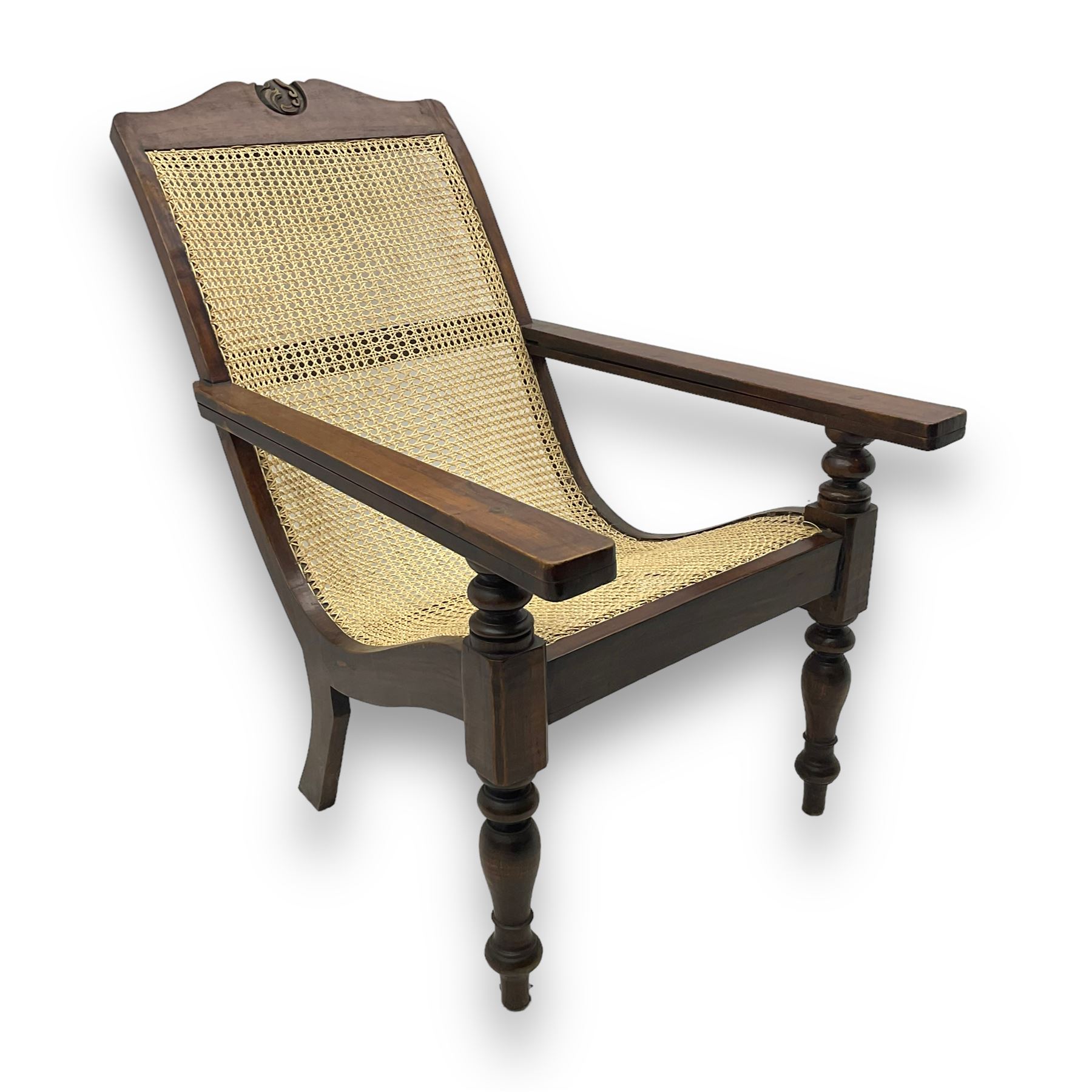 Late 19th century caned plantation chair, shaped top rail with carved central motif over caned back and seat, extending armrests, on turned front supports